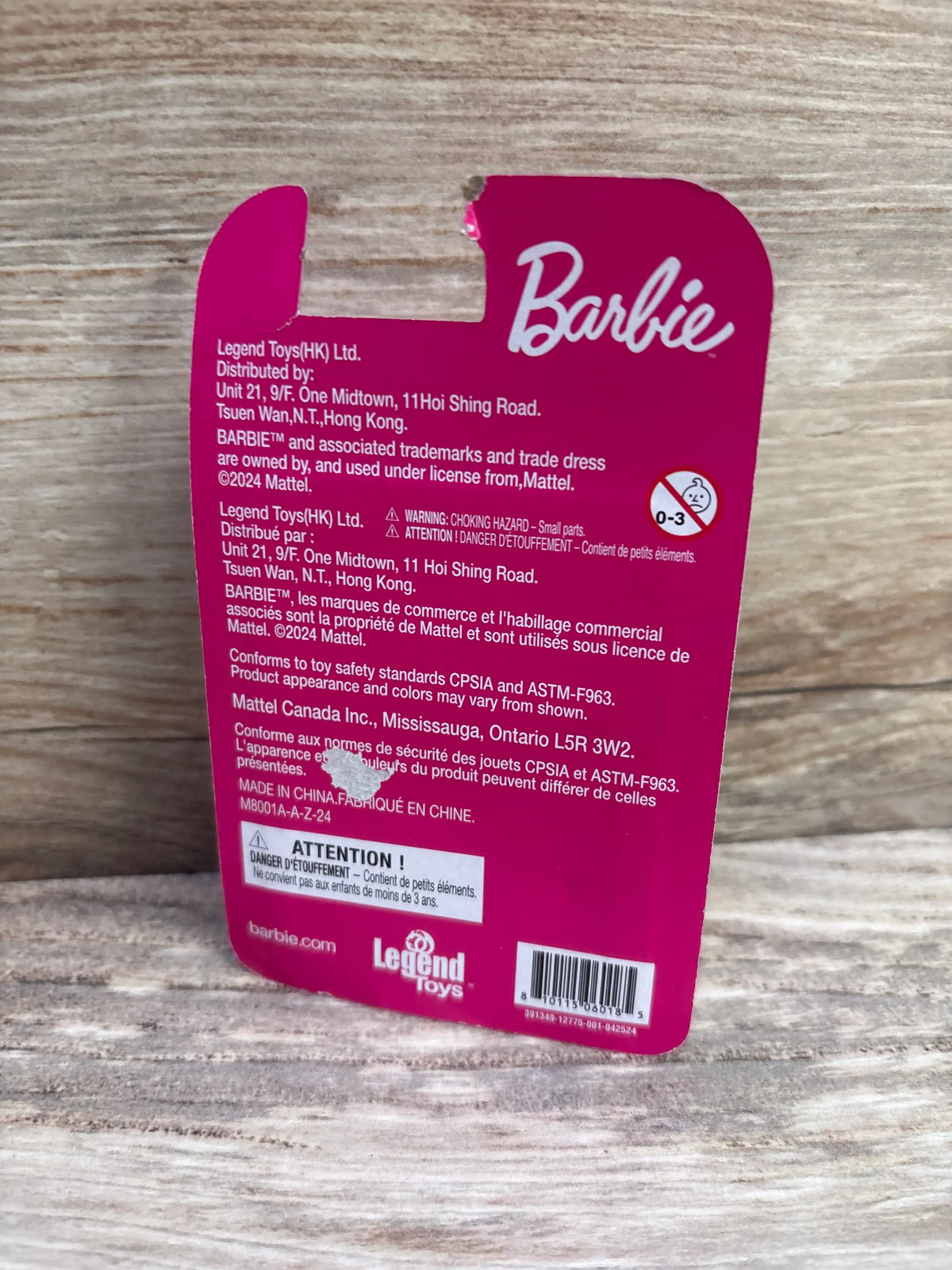 Back view of NEW Barbie mini figure packaging showing Barbie branding and a small-parts choking hazard warning on a wood surface