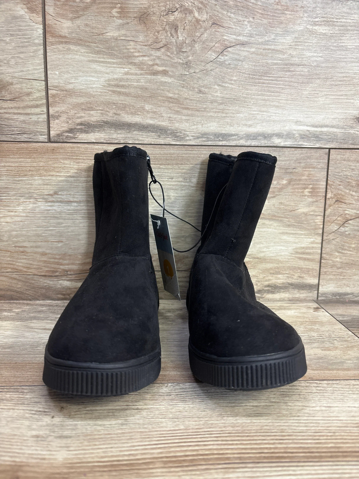Front view of NEW Cat and Jack Holland shearling-style boots in black suede with platform sole and hangtag on wood plank floor
