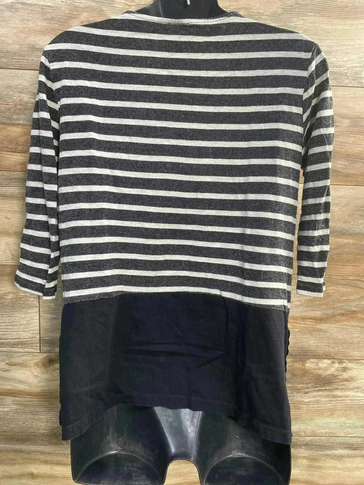 Back of maternity striped top with gray and black stripes, solid black lower panel and elbow length sleeves on wood backdrop