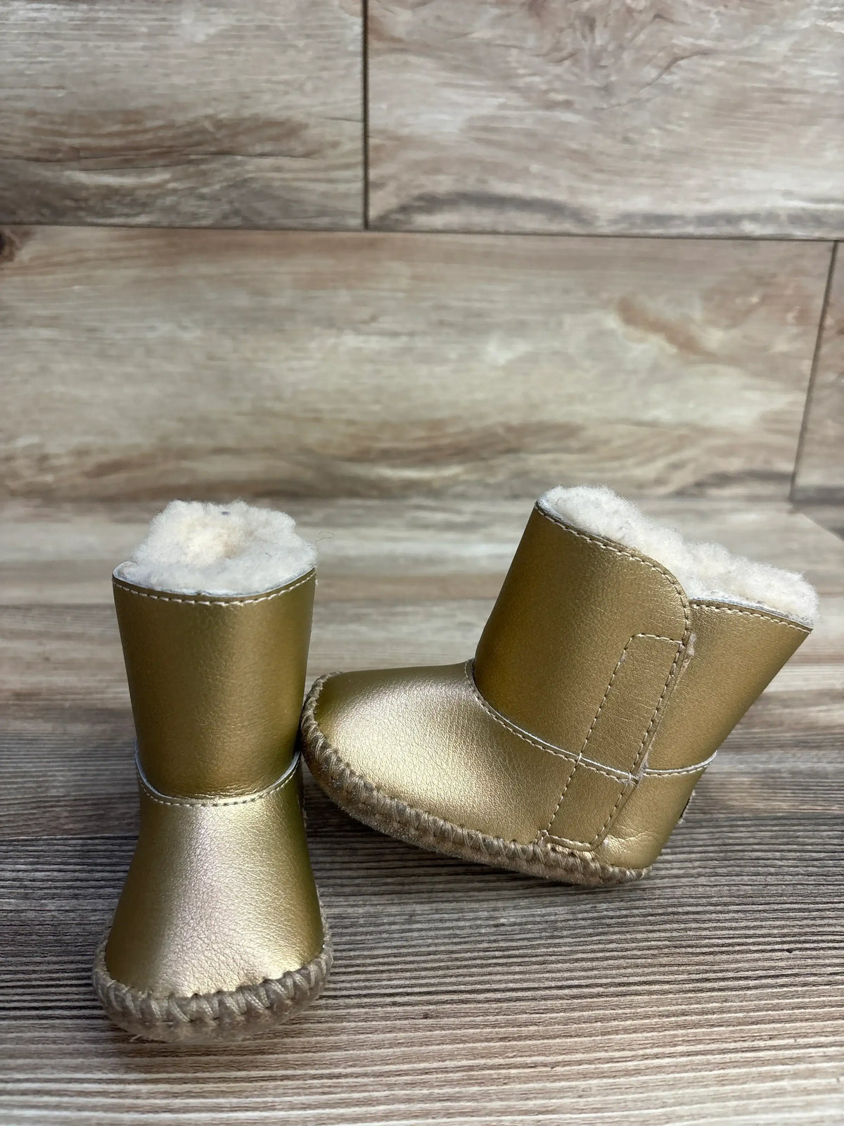 Pair of gold baby boots with white fleece lining on wooden surface and background