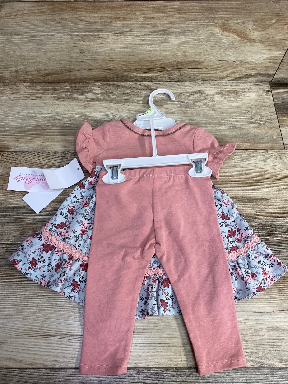 Pink baby outfit with short-sleeve top and floral skirt with pink leggings on wooden floor