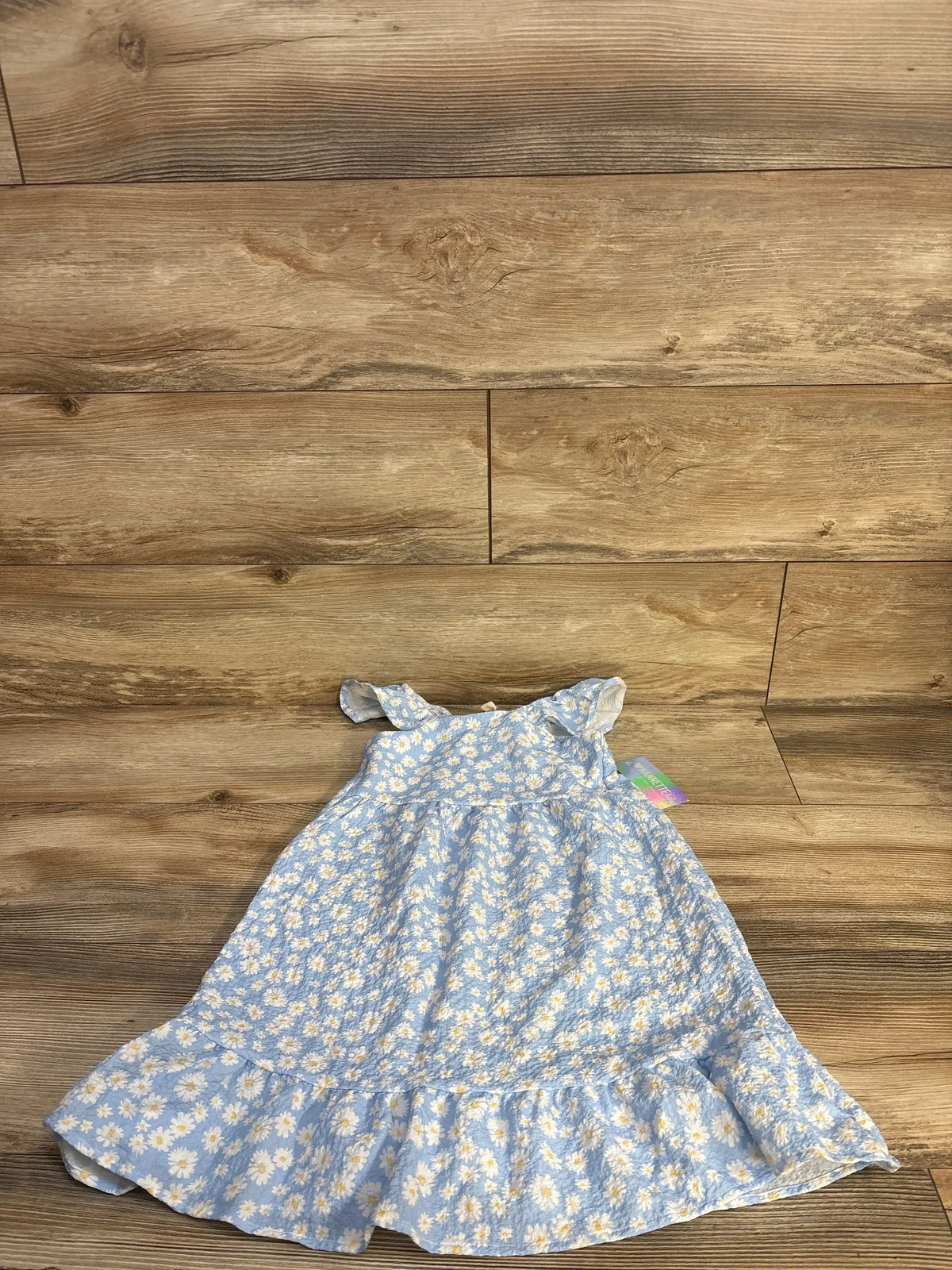 Flat lay of NEW Nannette Floral Sleeveless Dress sz 4T showcasing blue daisy print with ruffled hem on wood plank floor