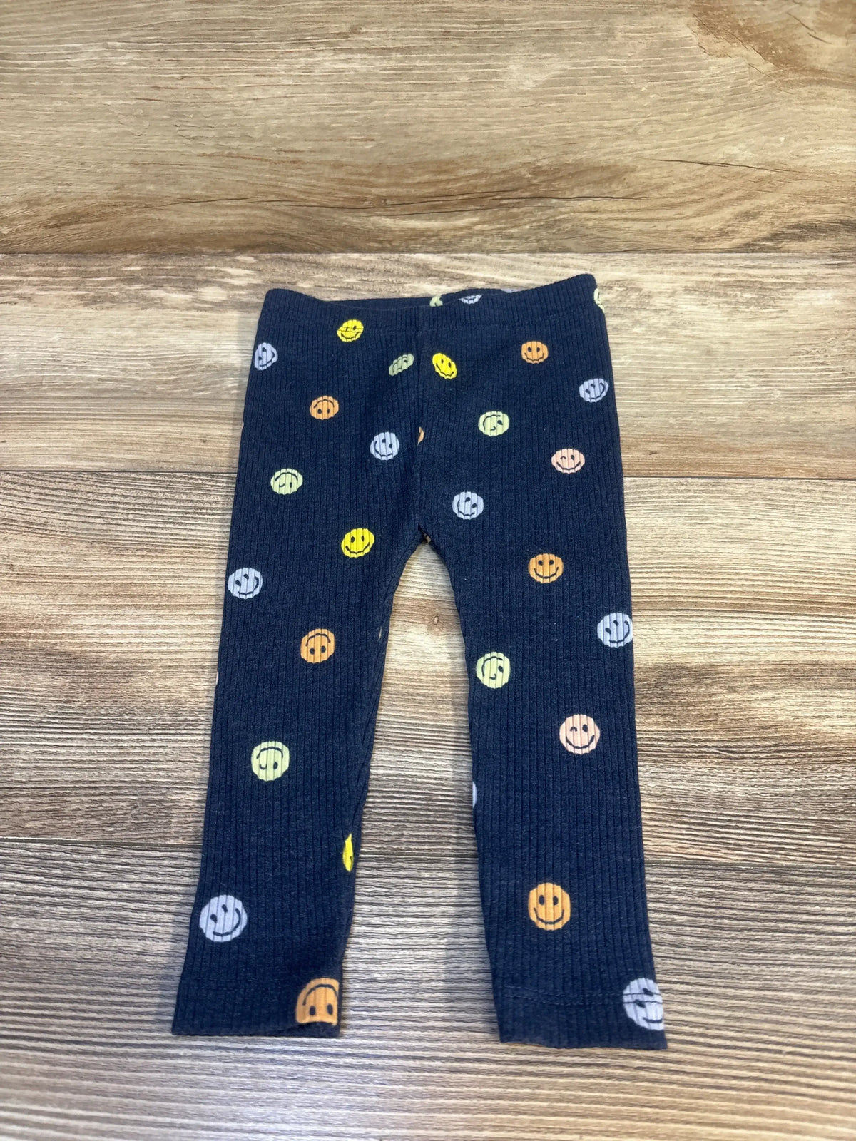 Flat lay of navy baby leggings showcasing multicolored smiley-face print and ribbed texture on wood background