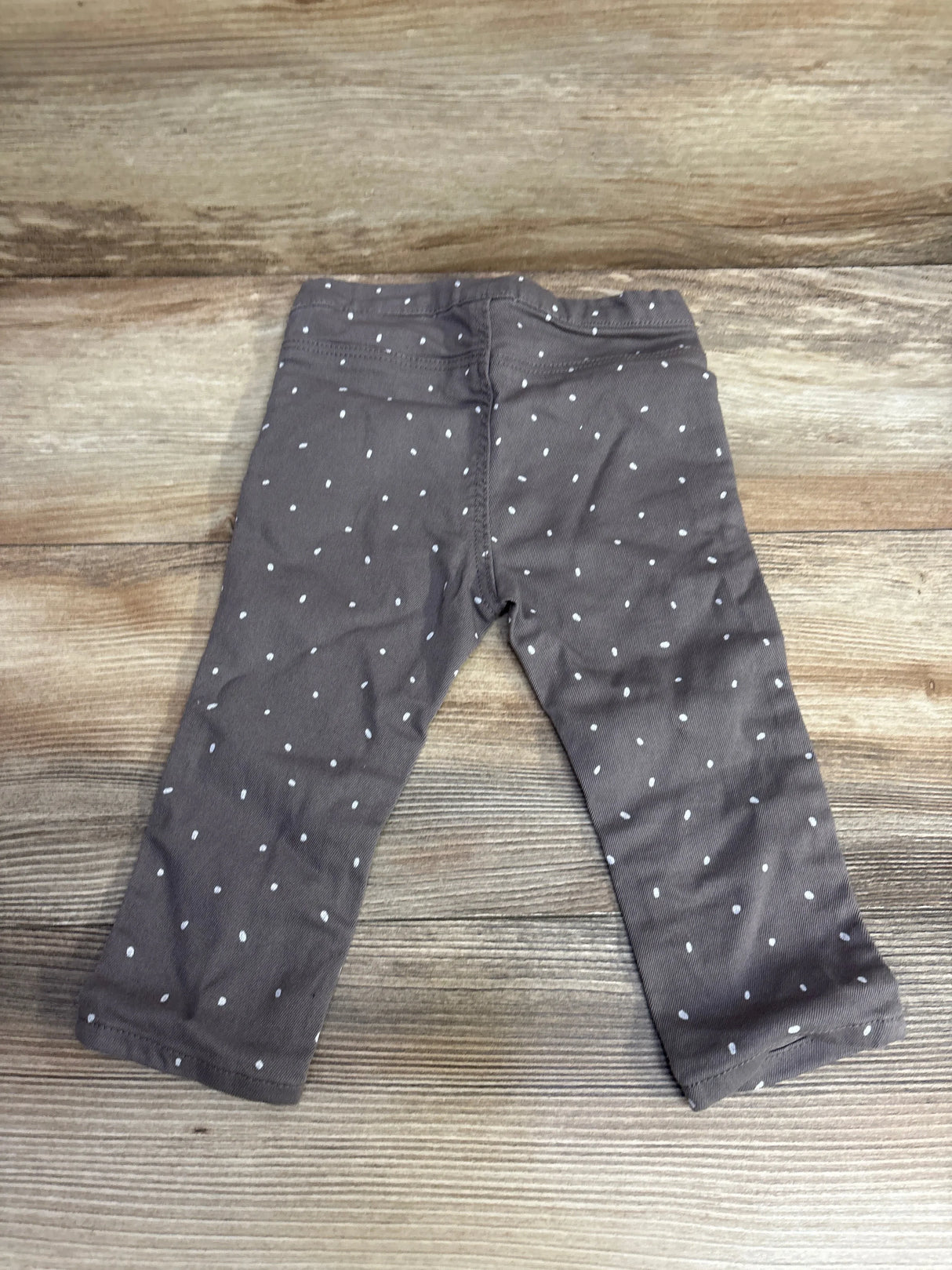 Flat lay of toddler grey pull-on denim-style pants (12 months) showing small white polka dots and elastic waistband on wood background