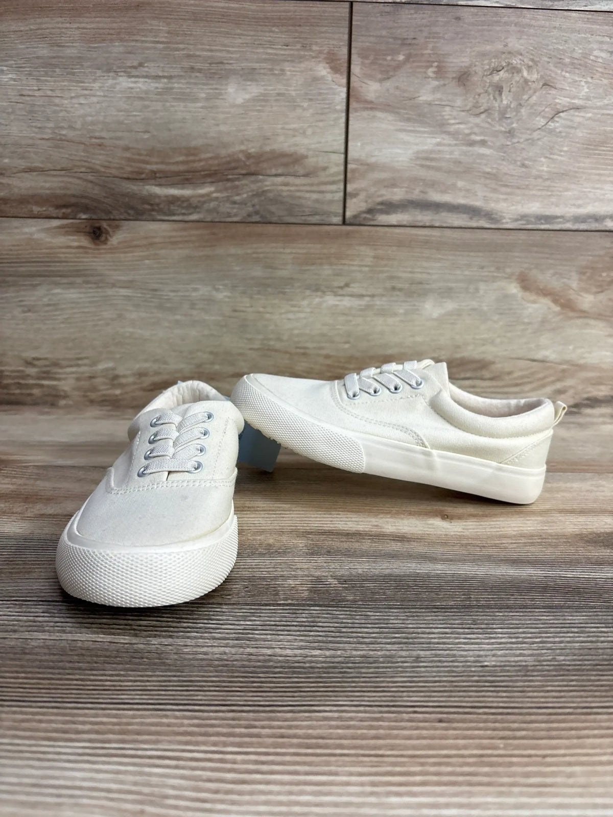 Front three-quarter of Cat and Jack Tyler off-white slip-on toddler sneakers showing canvas upper and rubber sole on wood floor
