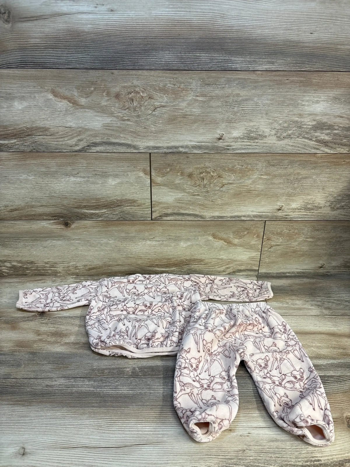 Flat lay of beige H&M x Disney Bambi sweatshirt and pants set showcasing velvet fabric and all-over print on wood floor