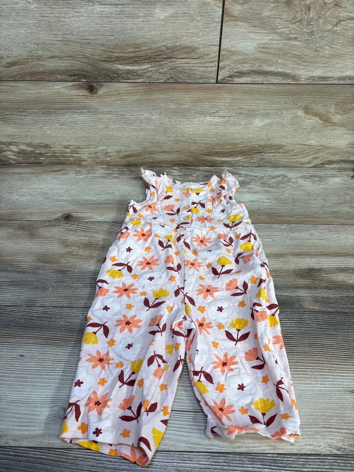 Flat lay of pink floral baby jumpsuit showing ruffle cap sleeves and elastic waist with wood floor background