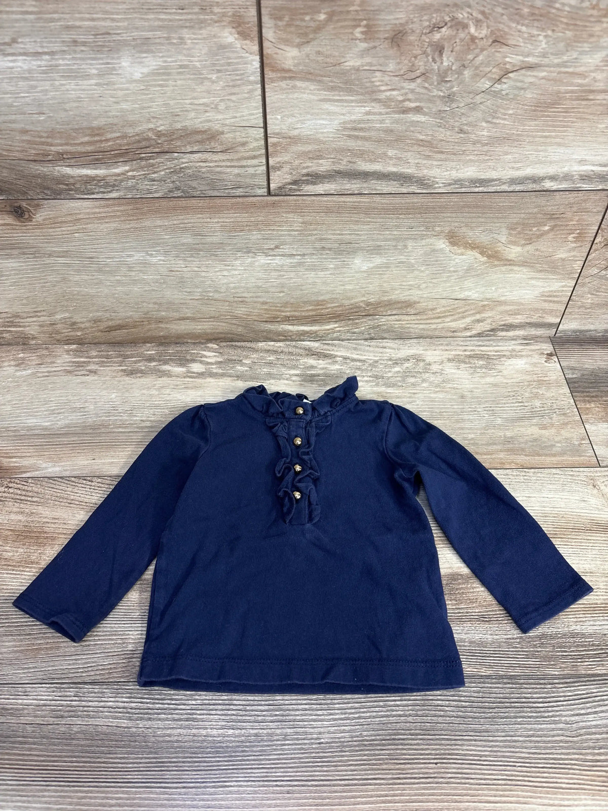 Navy blue long sleeve toddler shirt with ruffle trim and buttons, on wood floor