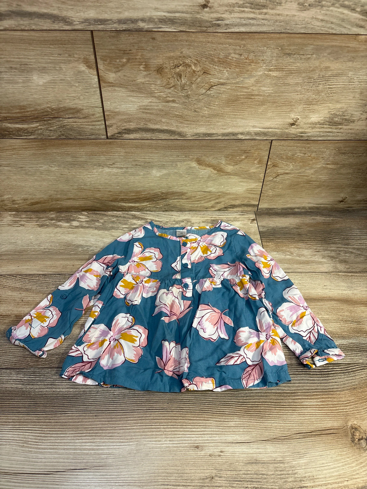 Flat lay of blue button-front viscose top (2T) with long sleeves and pink-and-white floral print on wood background