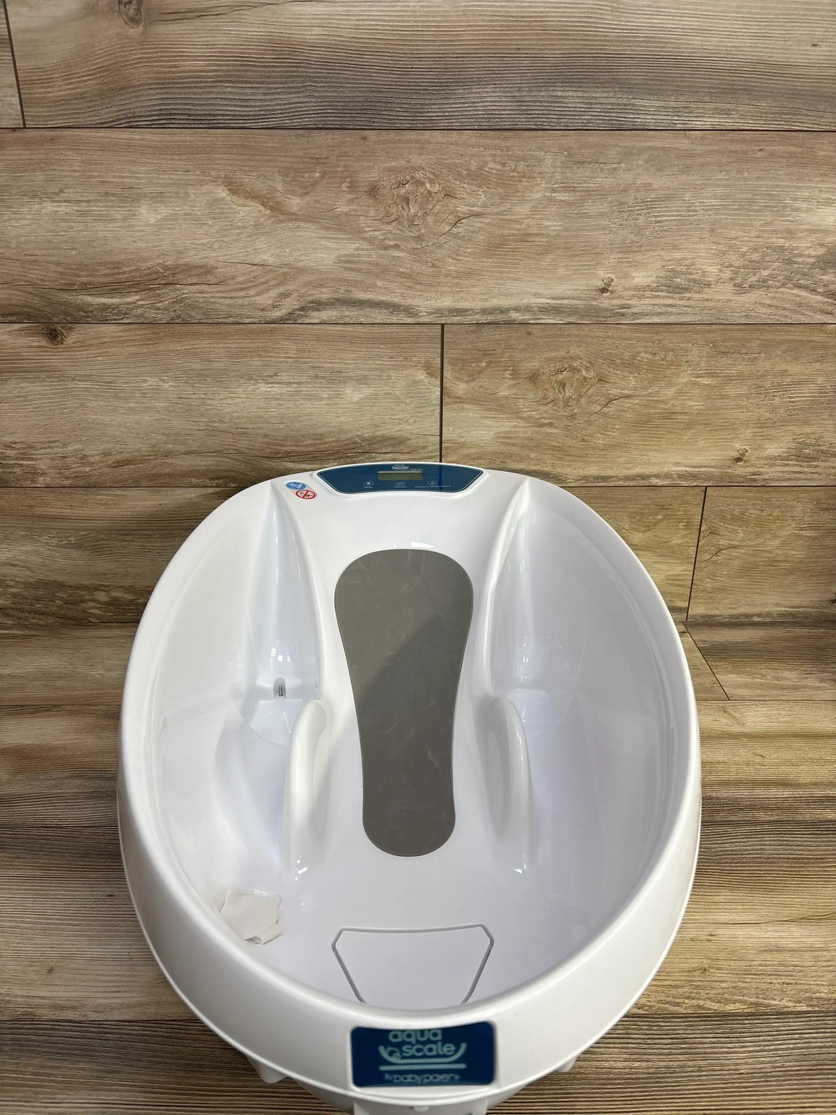 Top view of AquaScale 3-in-1 infant tub showing built-in digital scale and contoured baby support on wood floor background