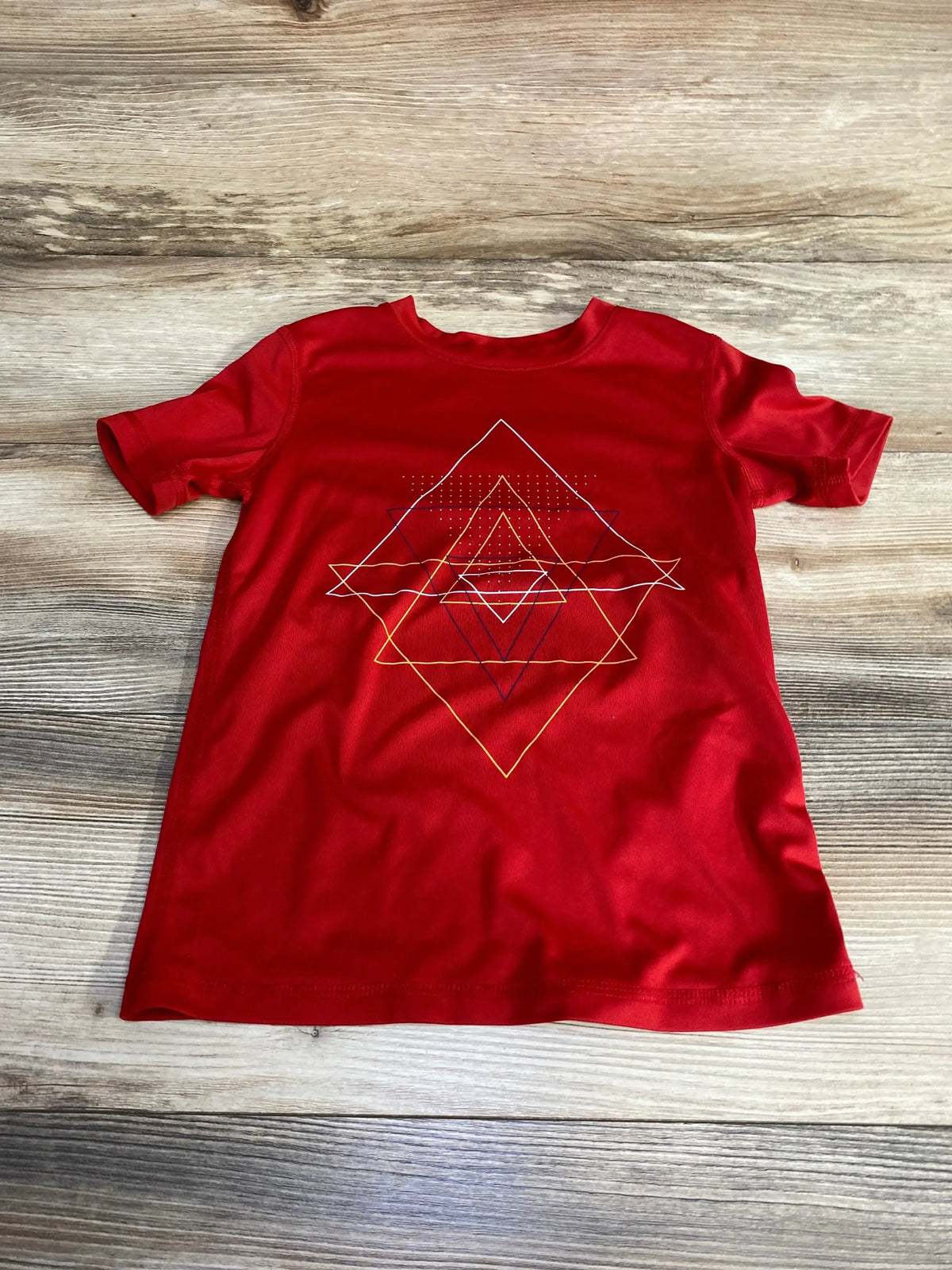 Front view of red All In Motion toddler short-sleeve shirt showing layered geometric diamond graphic on wood background