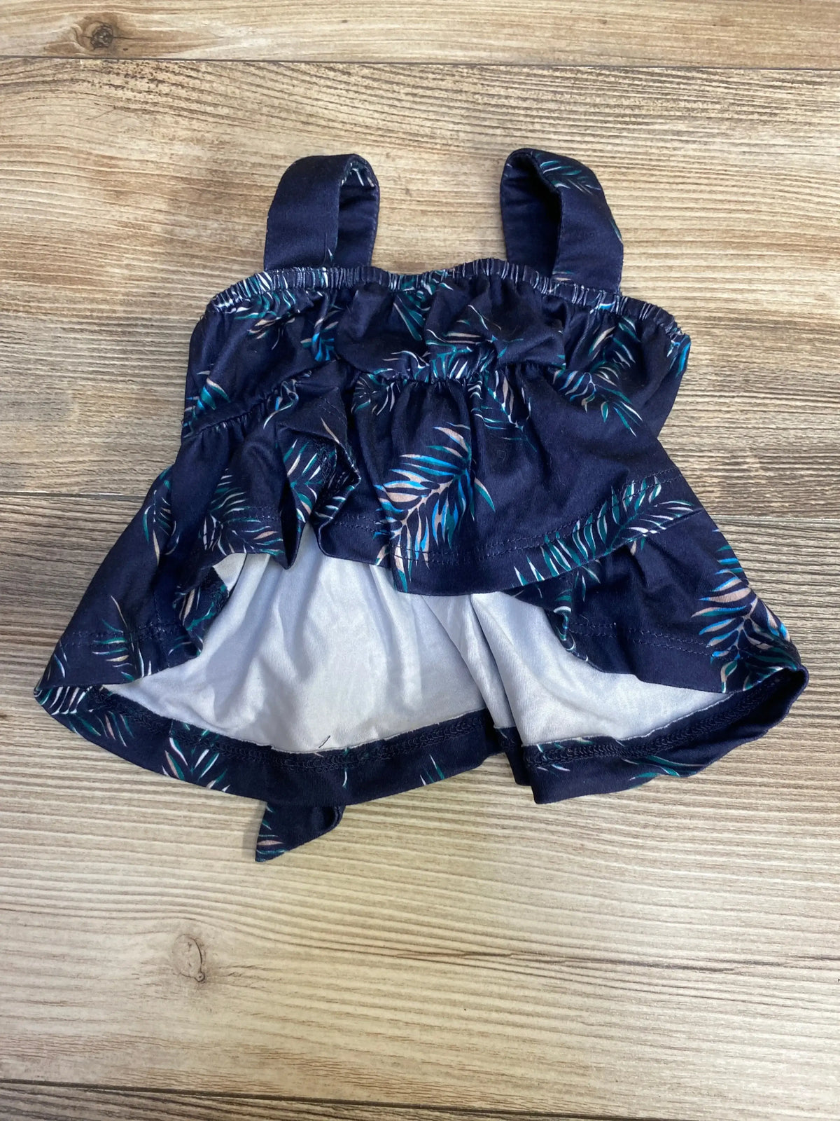 Front view of Baileys Blossoms Sleeveless Top in navy with teal palm leaf print showcasing tank straps and ruffle tier hem on wood plank floor