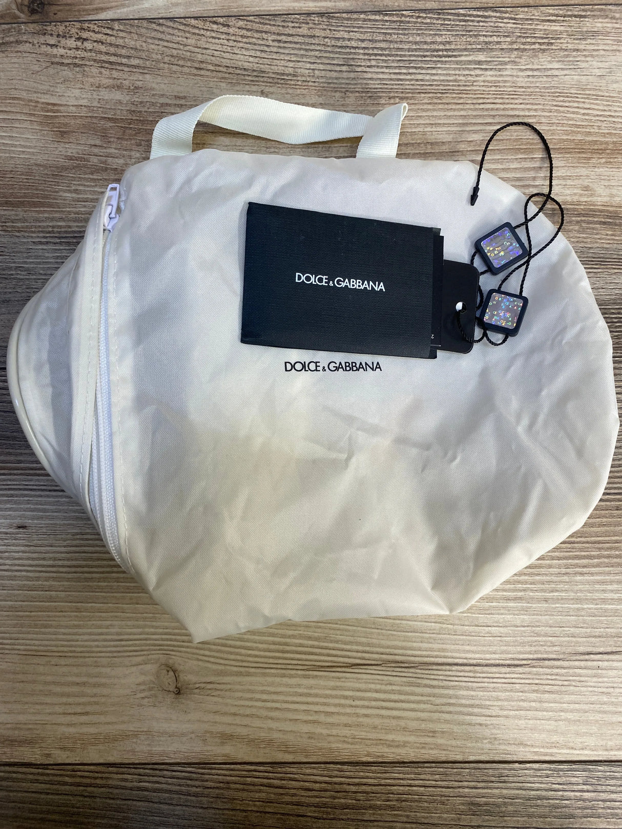 White Dolce & Gabbana dust bag with tags and card on wood background, kids fashion accessory