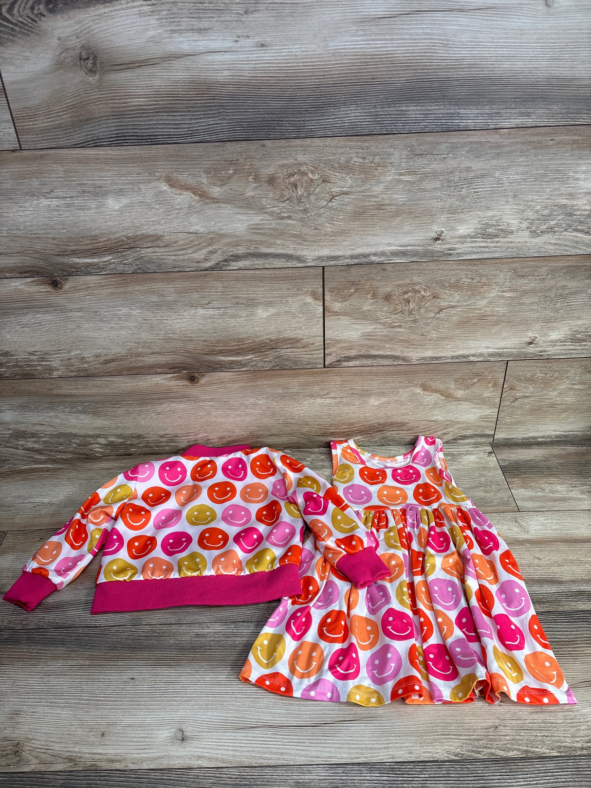 Colorful toddler dress and matching jacket with smiley face prints on wooden floor