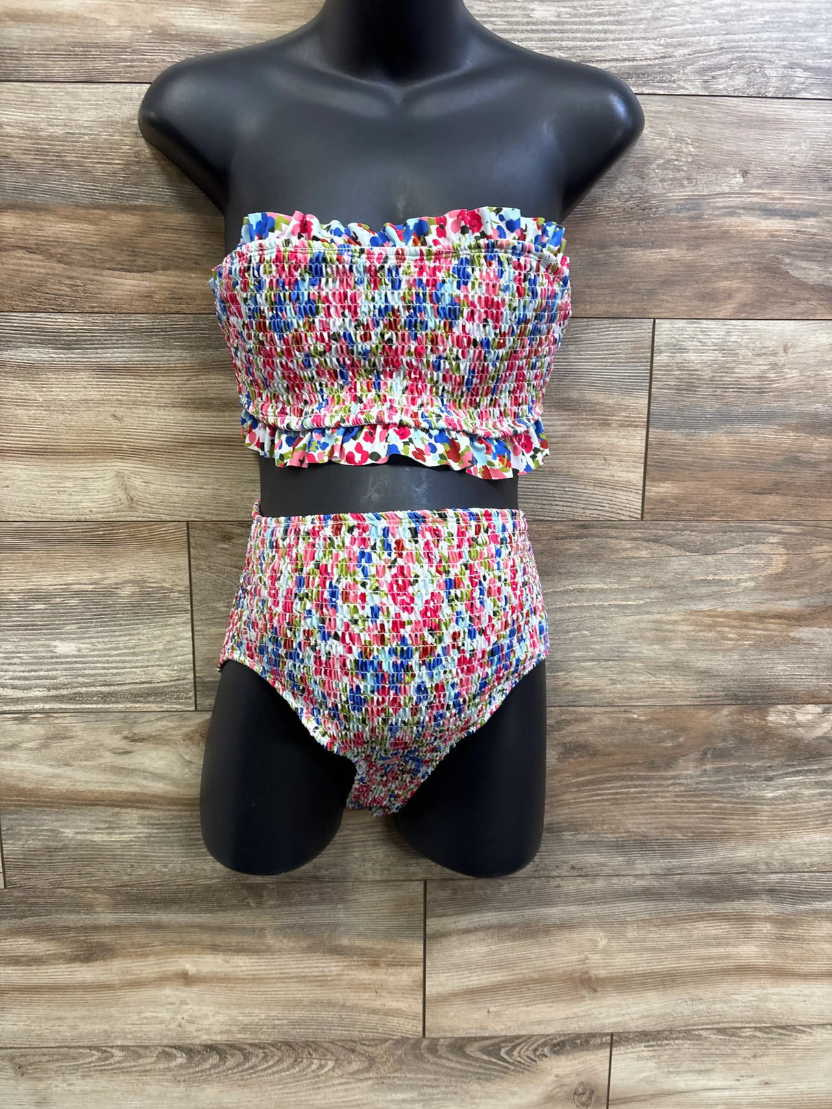 Front view of maternity smocked two-piece swimsuit, strapless ruffle top and high-waist smocked bottoms on wood background