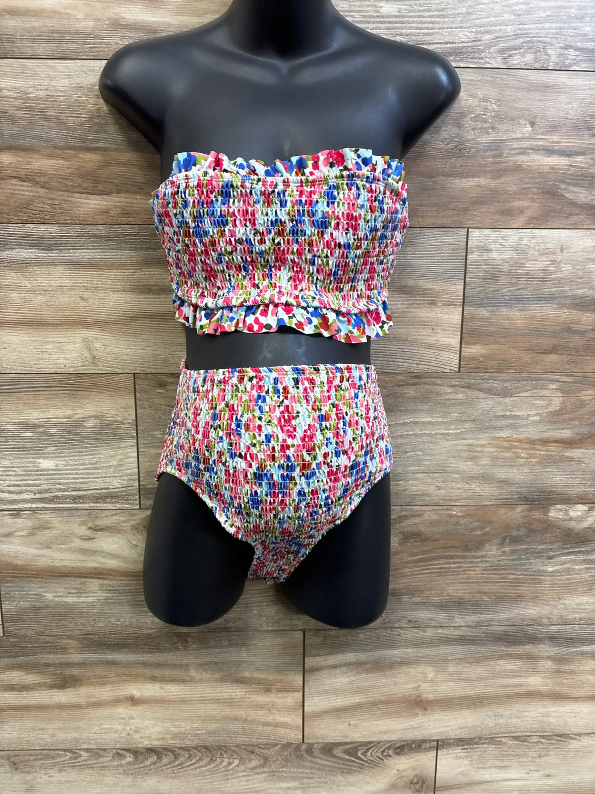 Front view of maternity smocked two-piece swimsuit, strapless ruffle top and high-waist smocked bottoms on wood background