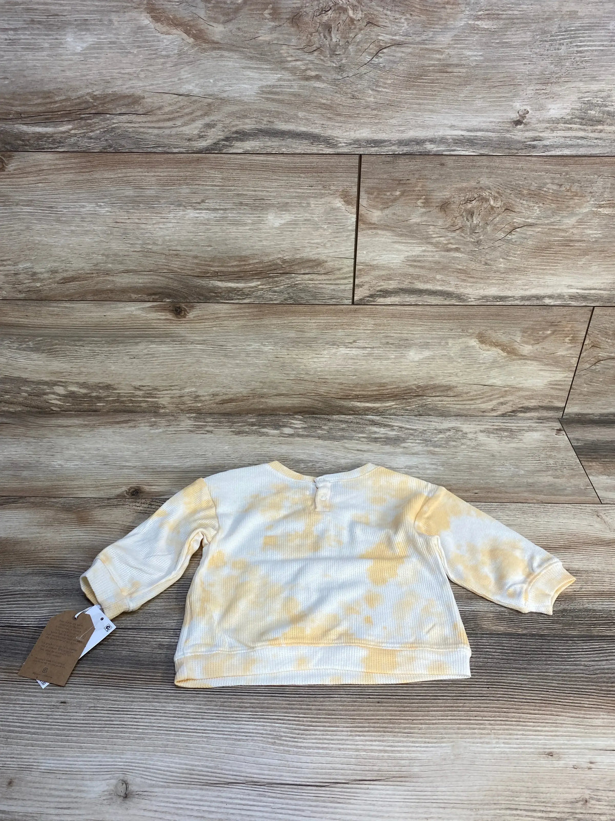 Back view of baby long sleeve sweatshirt showcasing yellow and white tie-dye knit with hangtag on wood plank floor
