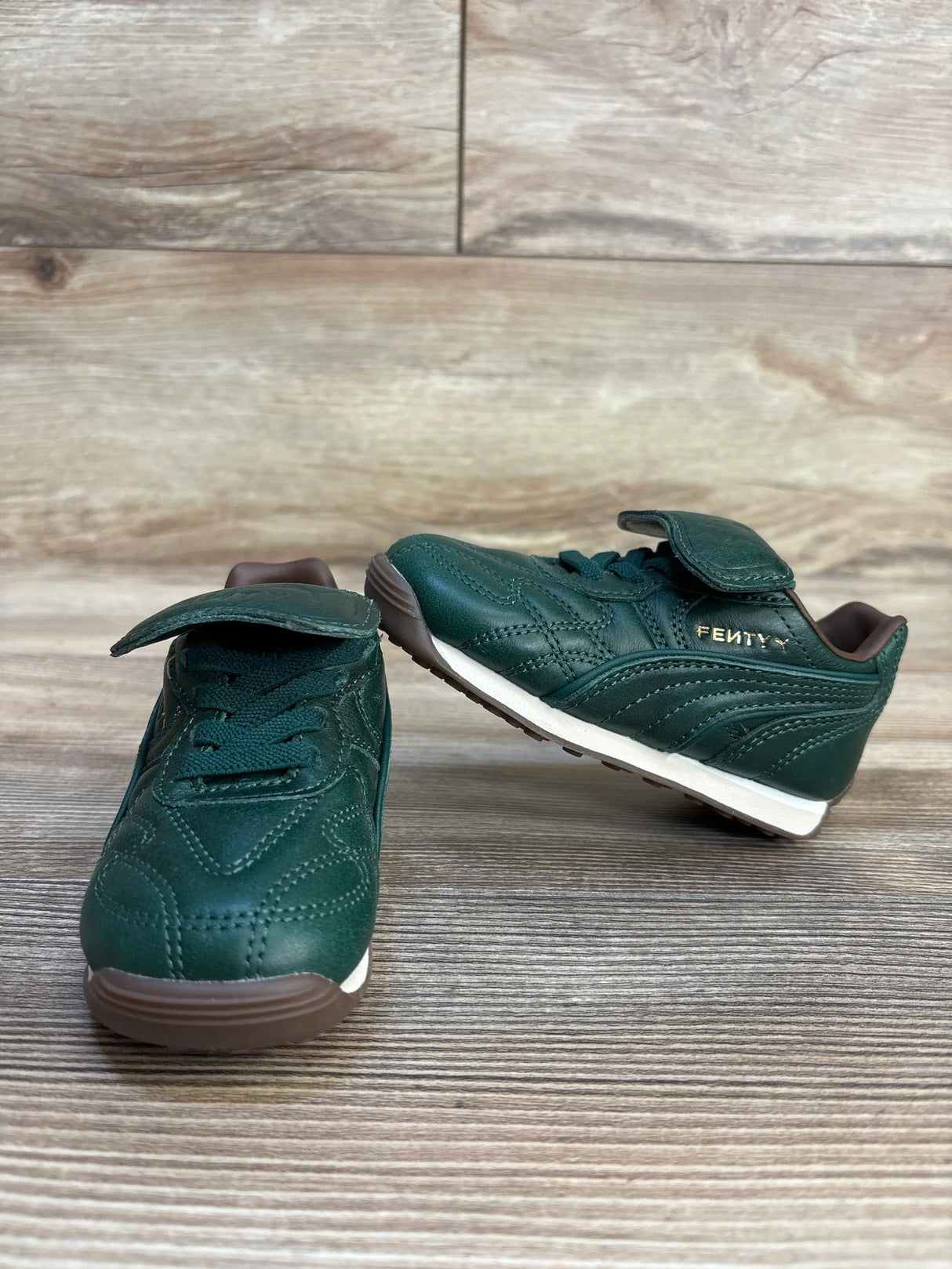 Green toddler sneakers with velcro straps and Fenty branding, displayed on wood floor