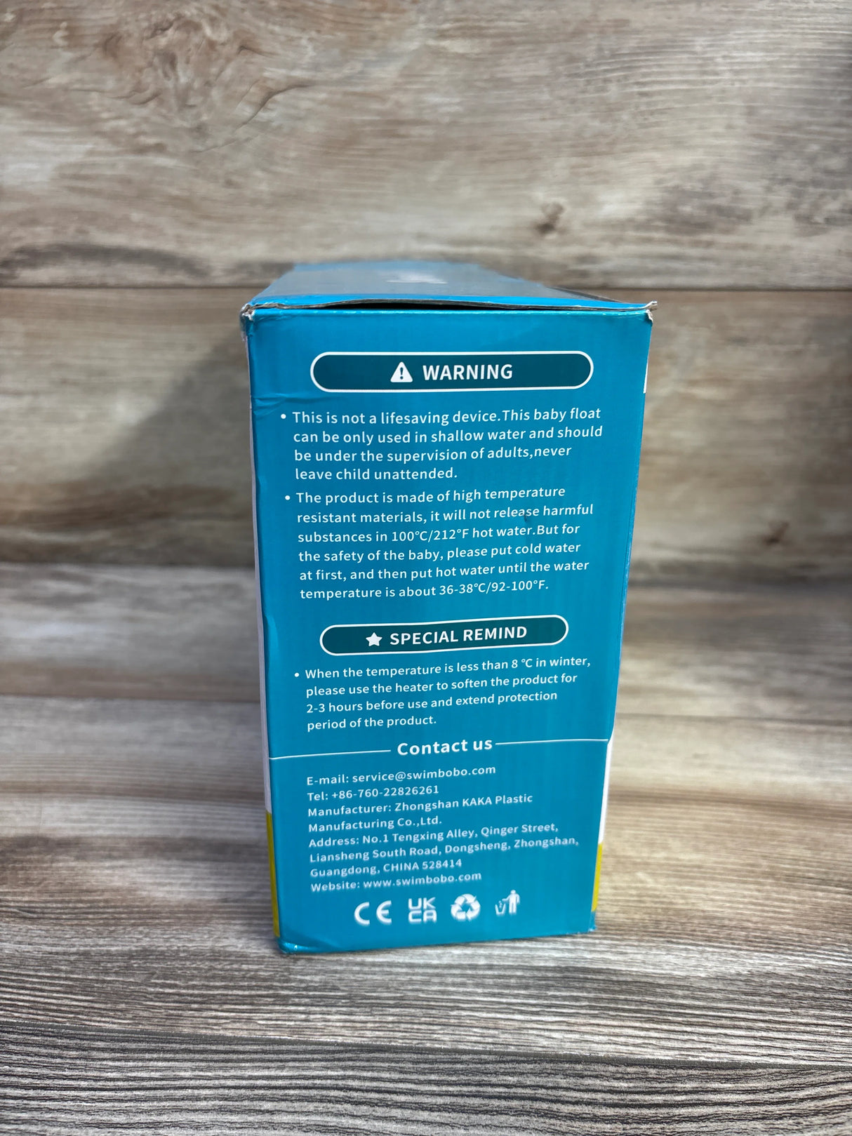 Back of SwimBoBo inflatable baby tub box showing warning and care instructions on teal packaging against wood background