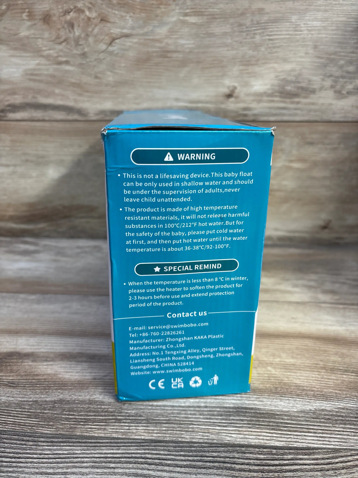 Back of SwimBoBo inflatable baby tub box showing warning and care instructions on teal packaging against wood background