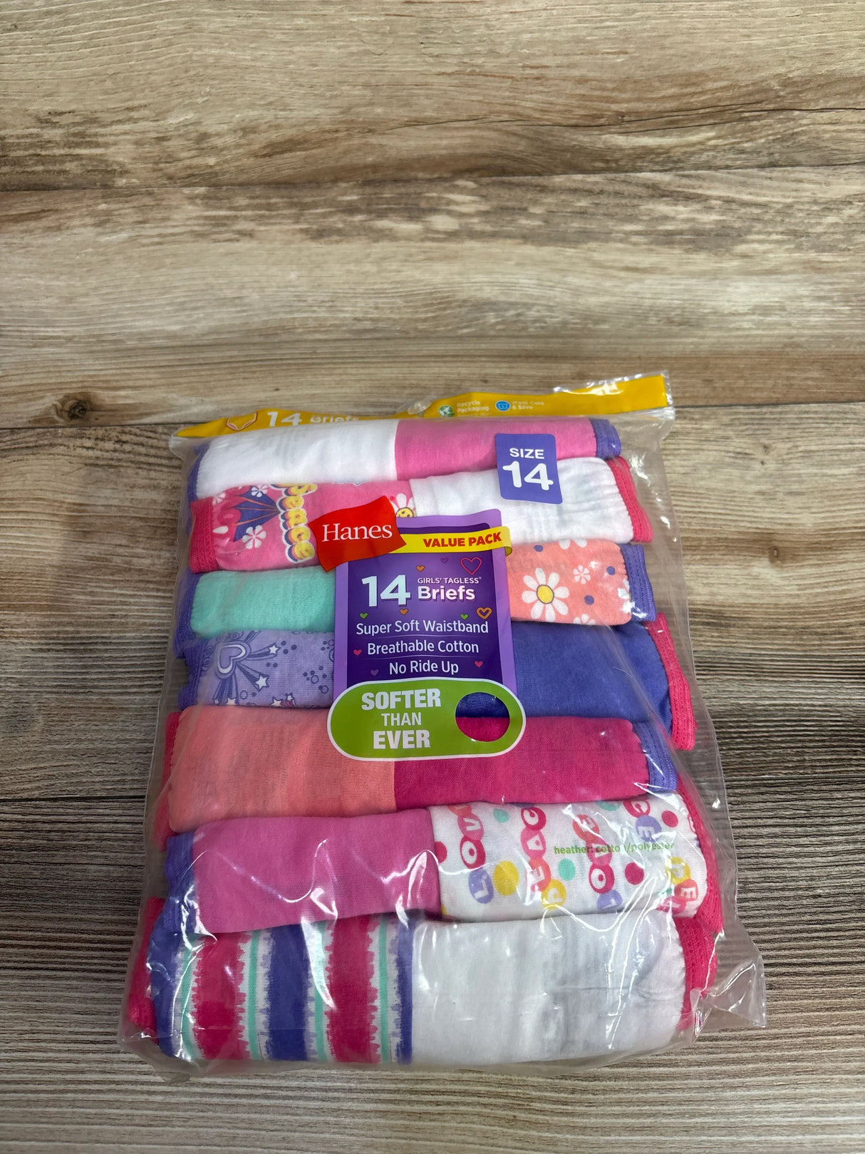 Top-down of Hanes 14-pack girls' tagless briefs showing assorted colorful patterns, size 14 label, on wood surface