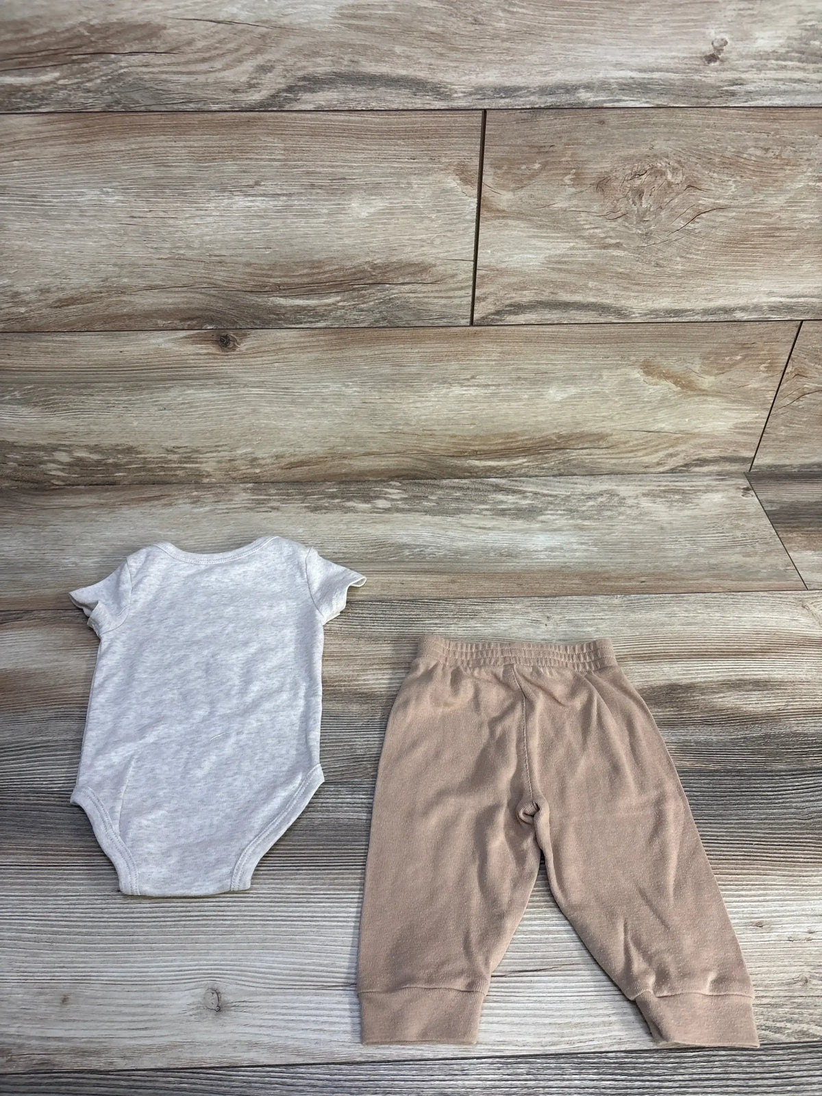 Flat lay of Nike 2-piece baby set: light heather bodysuit and beige pants, size 6M, on wood background