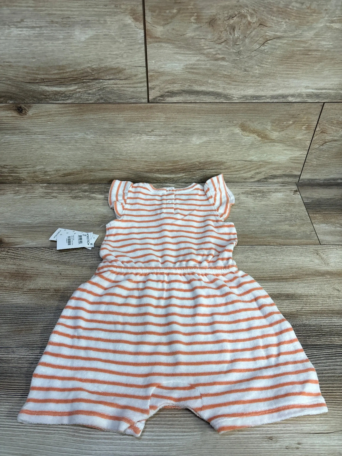 Top down view of Nordstrom terry romper with orange stripes, flutter sleeves and elastic waist on wood background
