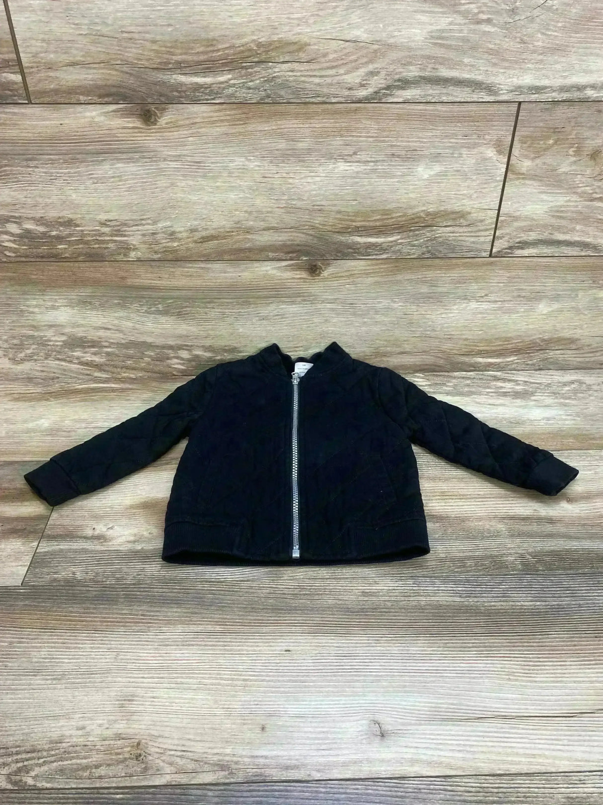 Flat lay of Wonder Nation Quilted Jacket Black sz 24m showcasing diamond quilted bomber with full zip and ribbed collar on wood plank floor