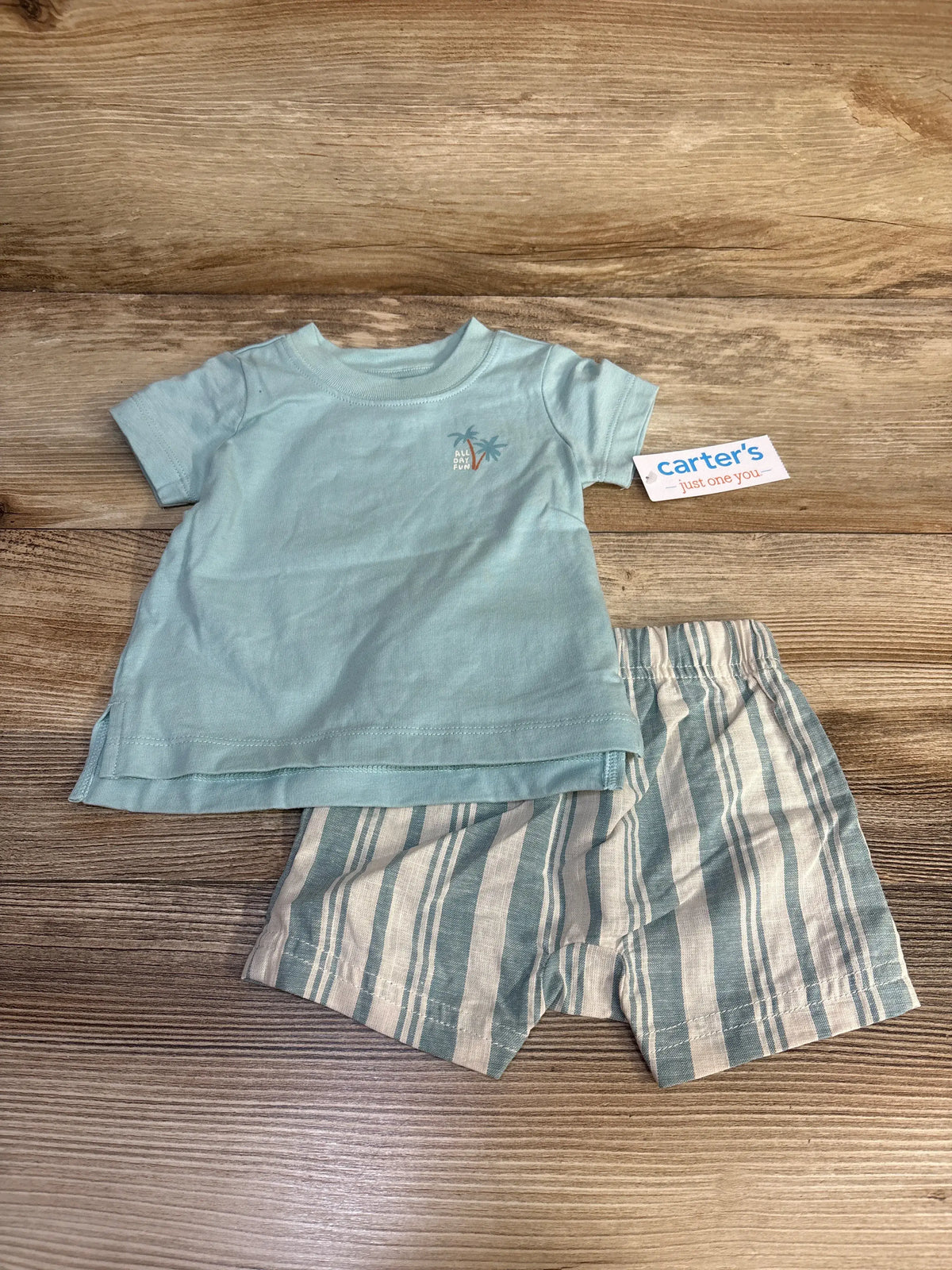 Front view of blue Just One You Surf’s Up two-piece baby outfit showcasing a surf-themed shirt and striped shorts on wood