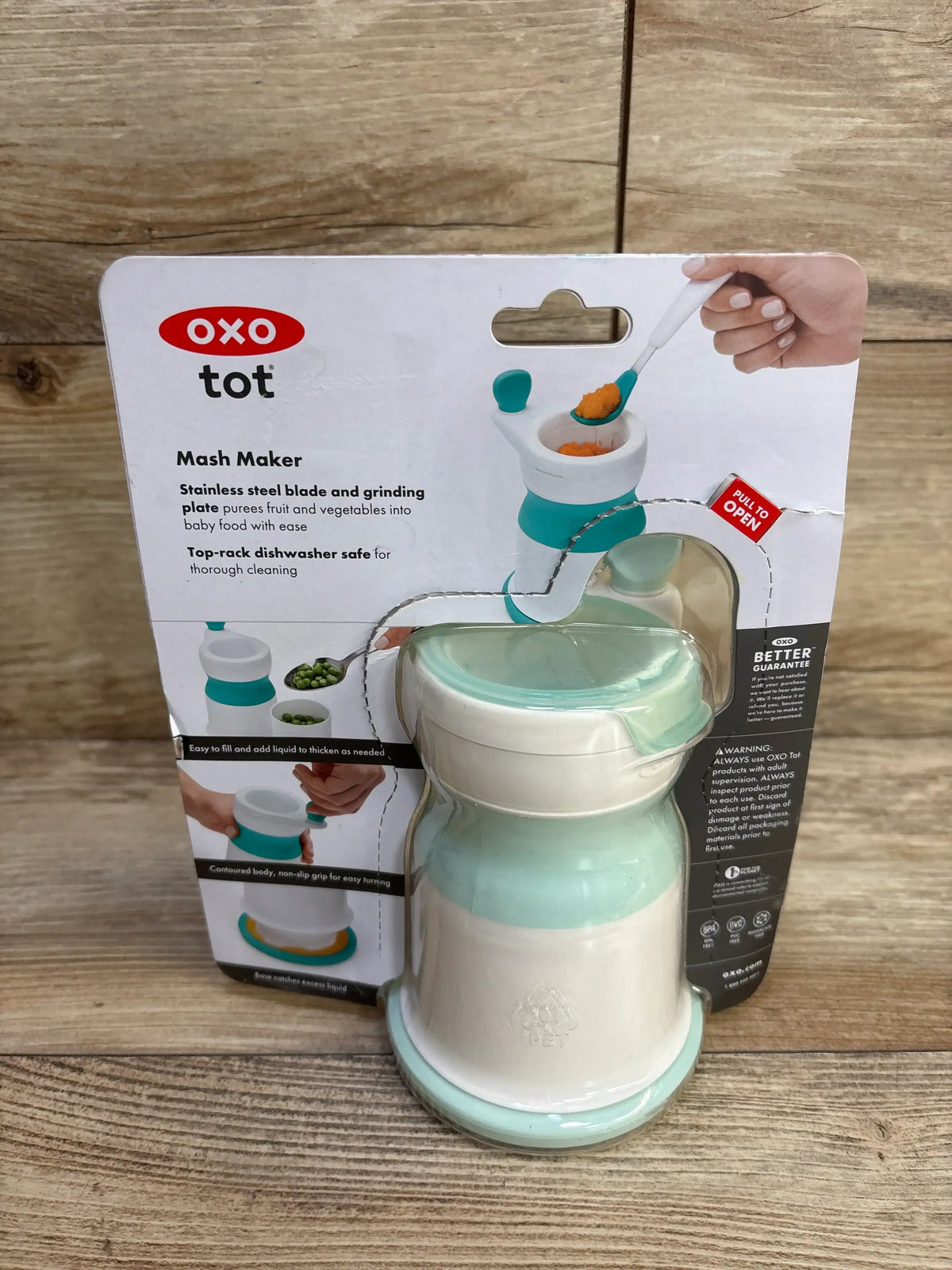 Front view of OXO Tot Mash Maker baby food mill in opal showing white and mint mill in original packaging on a wooden surface