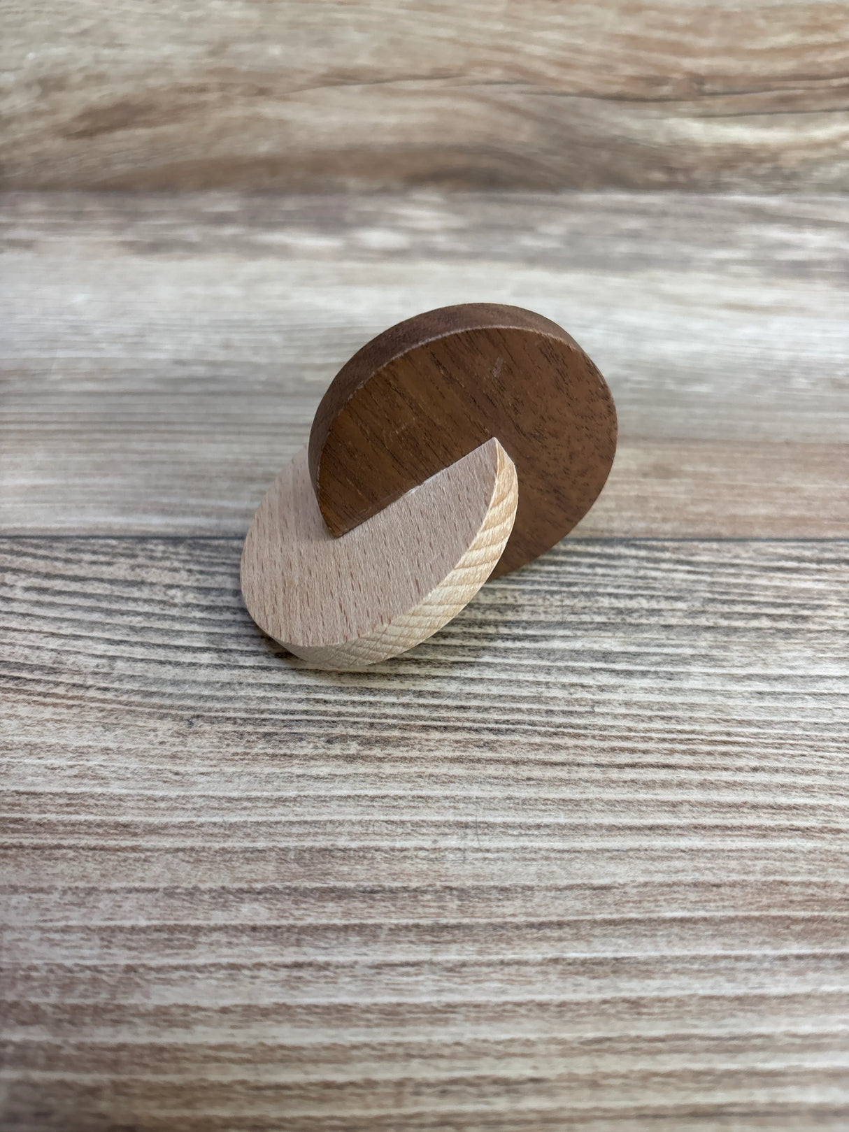 Two interlocking wooden discs on a wood grain surface, light and dark wood contrast.
