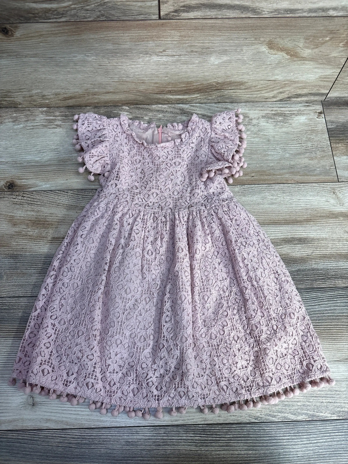 Pink toddler lace dress with pom-pom trim on wooden floor