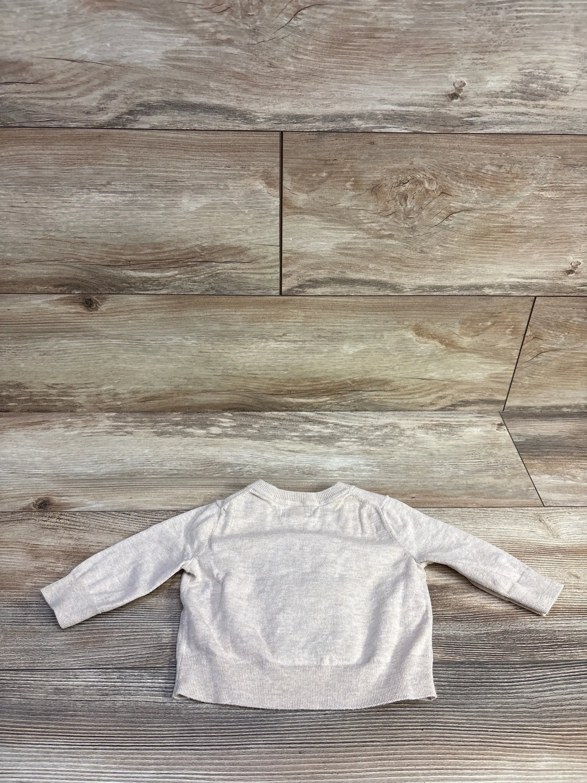 Back view of a beige Banana Republic intarsia-knit baby sweater on a rustic wood background.