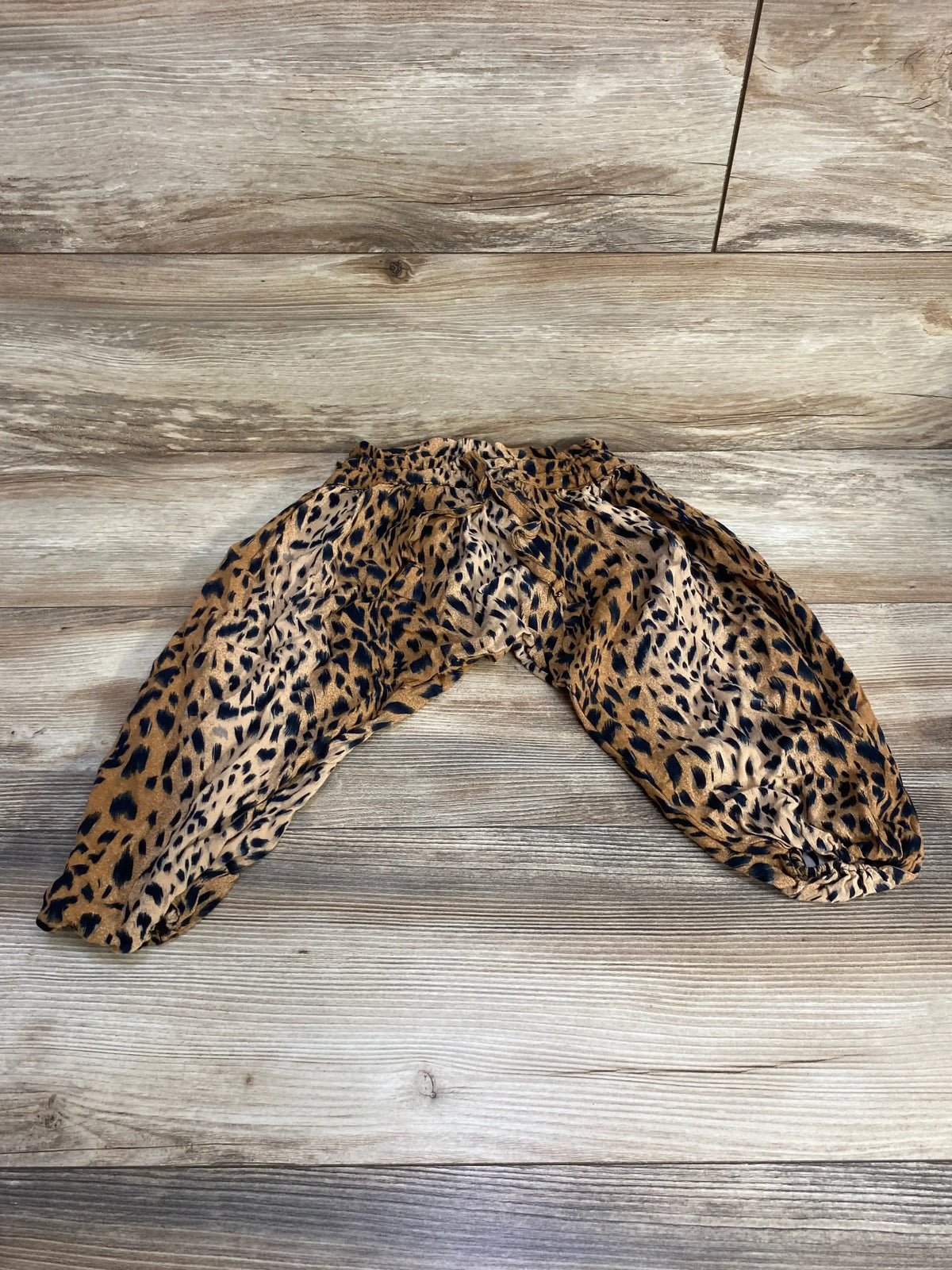 Flat lay of toddler harem pants showing brown leopard animal print, elastic waistband, and gathered ankles on wood background