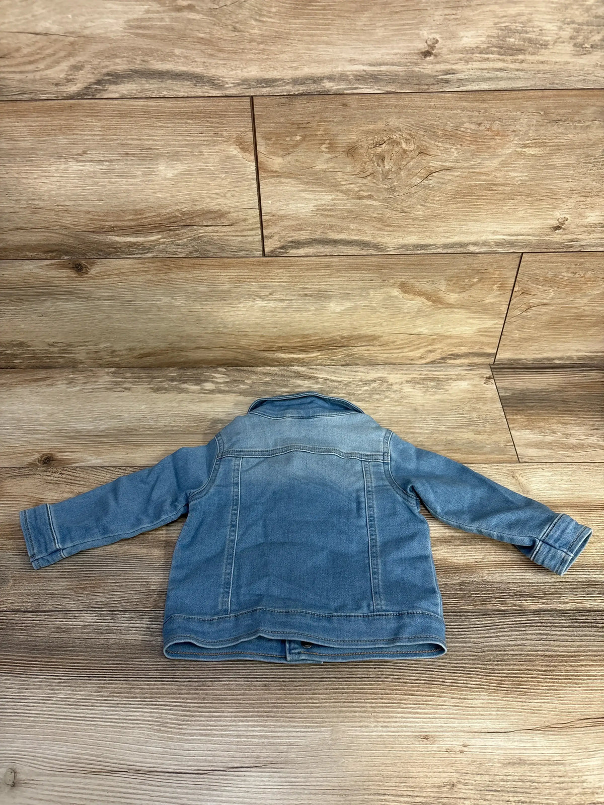 Back view of Cat and Jack toddler denim jacket, 12 months, showing light blue wash and long sleeves laid flat on wooden floor