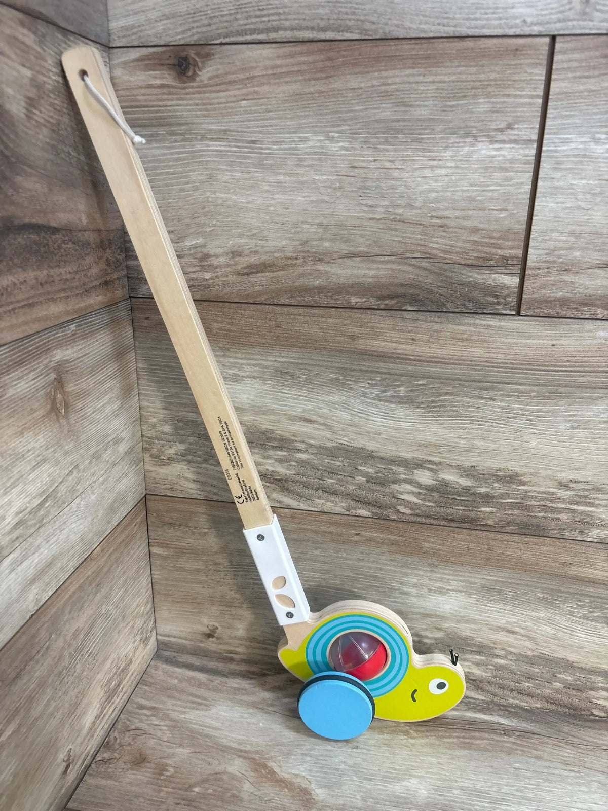Side view of Hape Snail Push Pal walking toy showing colorful bead shell and green wheels on wood floor