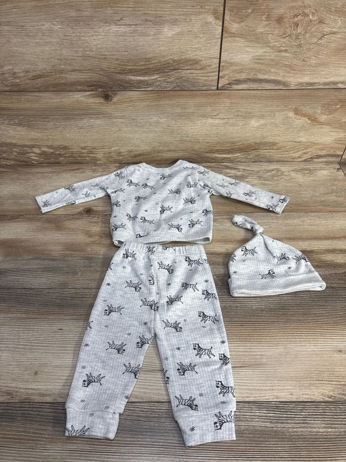 Top view of Kit and Pearl three piece grey zebra print set showing long sleeve shirt, pants, and knotted hat on wood floor