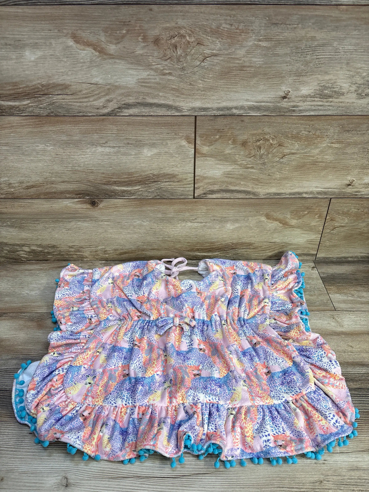 Front view of Cheeky Plum Ruffle Swim Cover in Wild One showcasing cinched waist and pom pom trim on wood flooring
