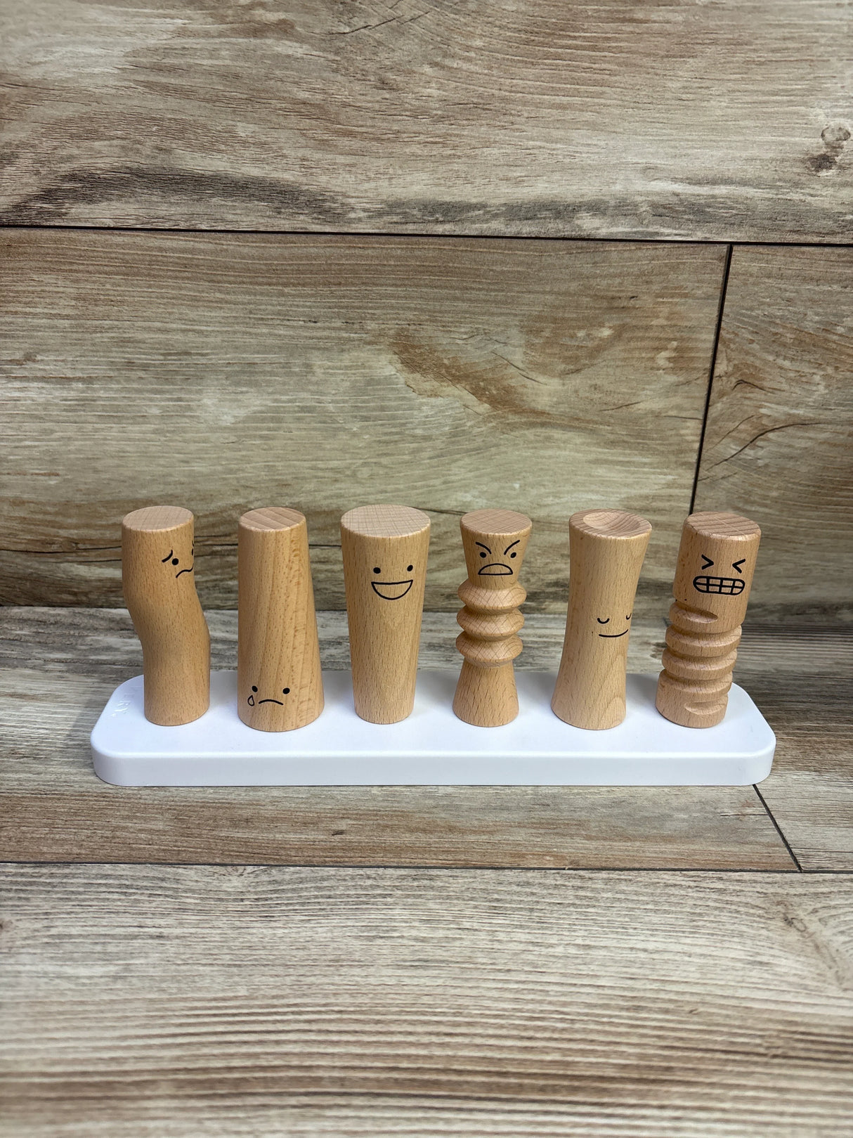 Front view of Lovevery wooden emotion dolls showing six carved figures with different facial expressions on a white base
