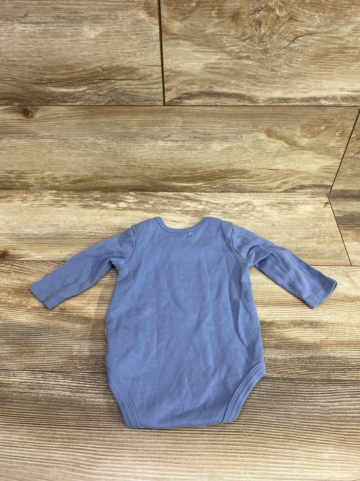 Blue long sleeve infant bodysuit for size 6-9 months on a wooden background.