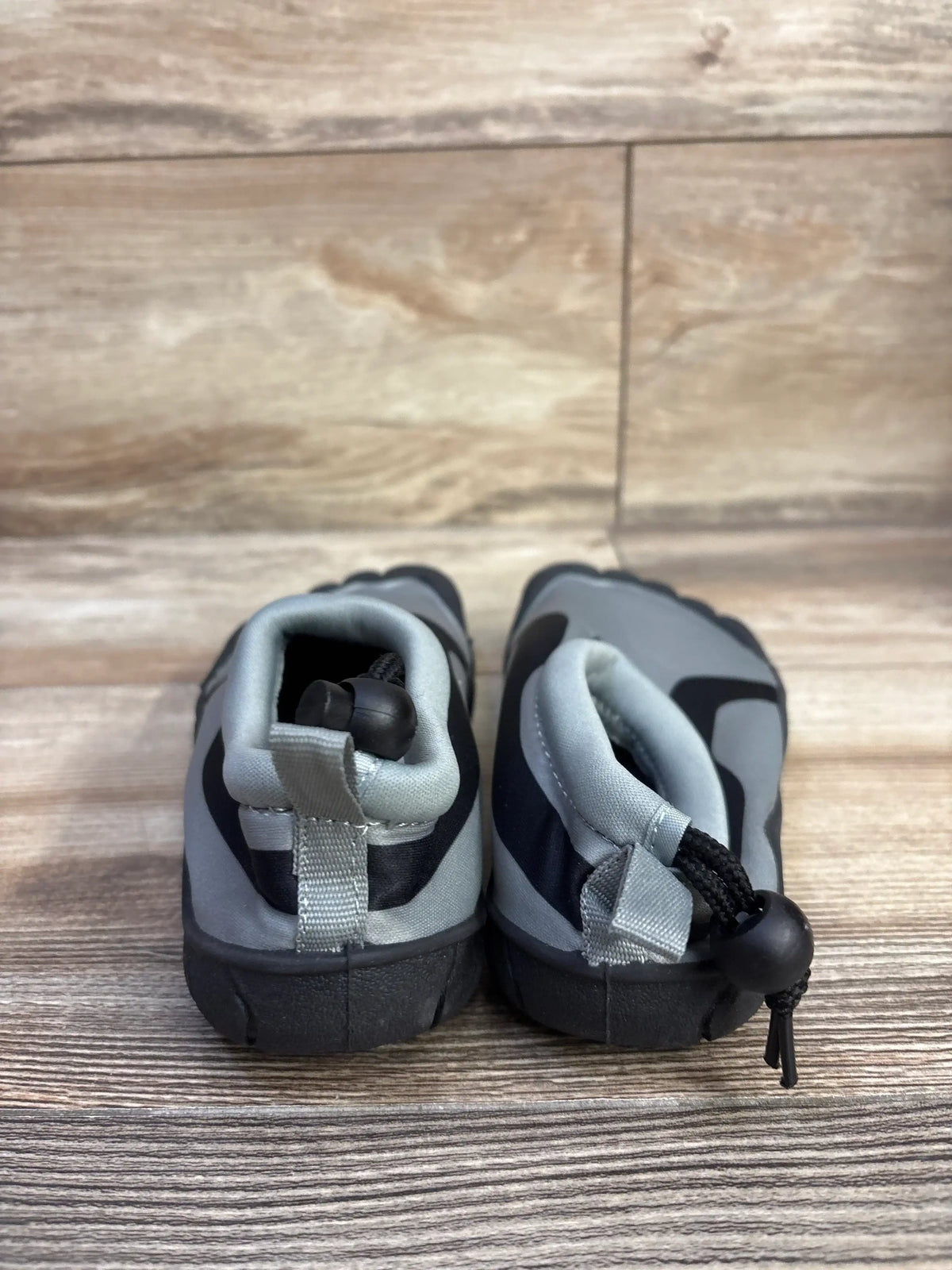 Rear view of grey RBX kids water shoes showing heel drawstring toggles and black rubber soles on wood background
