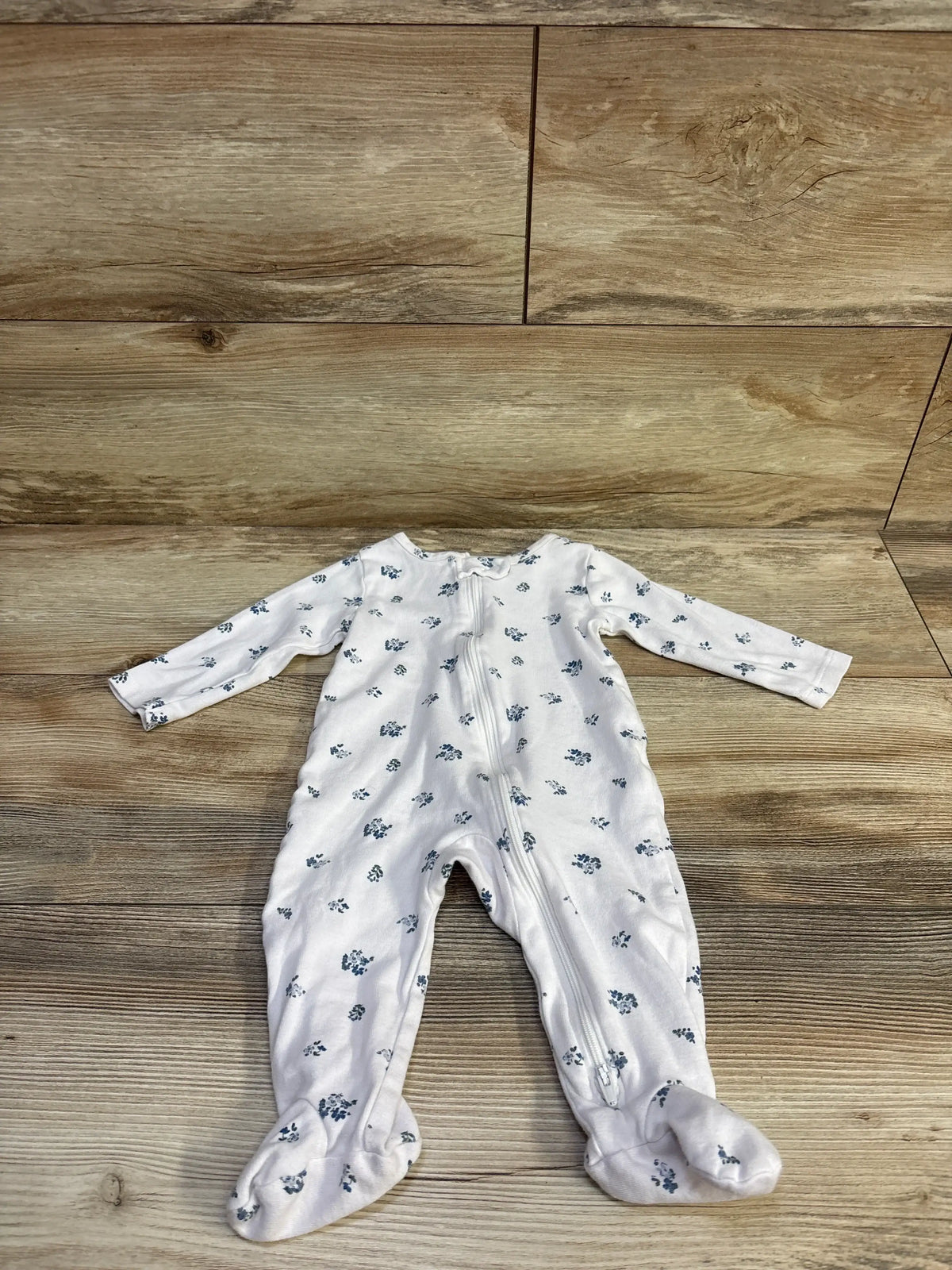 Front view of white floral footed sleeper showcasing long sleeves and front zipper on a wood floor