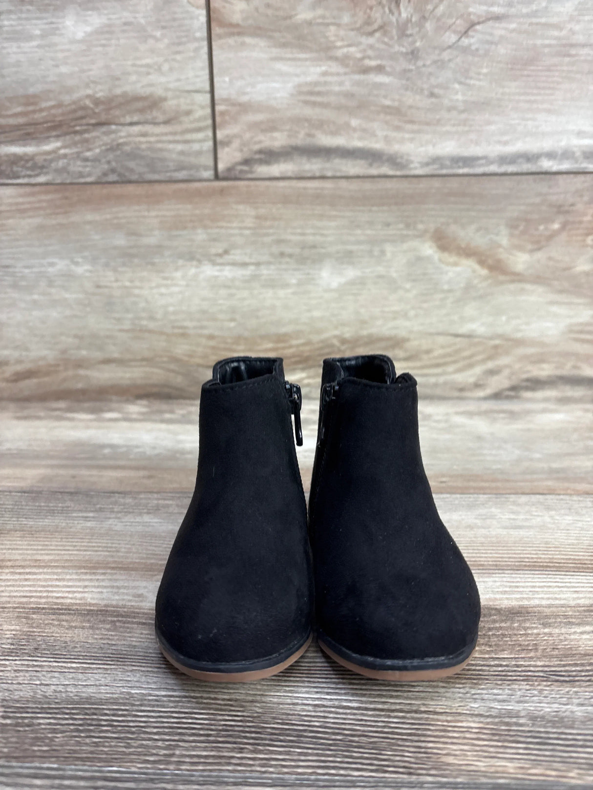 Pair of black suede toddler ankle boots with side zippers on wooden floor