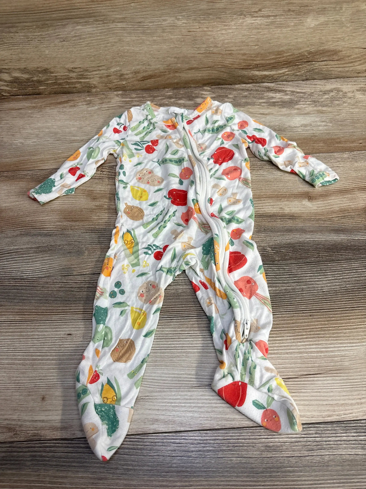 Flat lay of white Angel Dear footie with colorful vegetable print, front zipper and enclosed feet on wood background