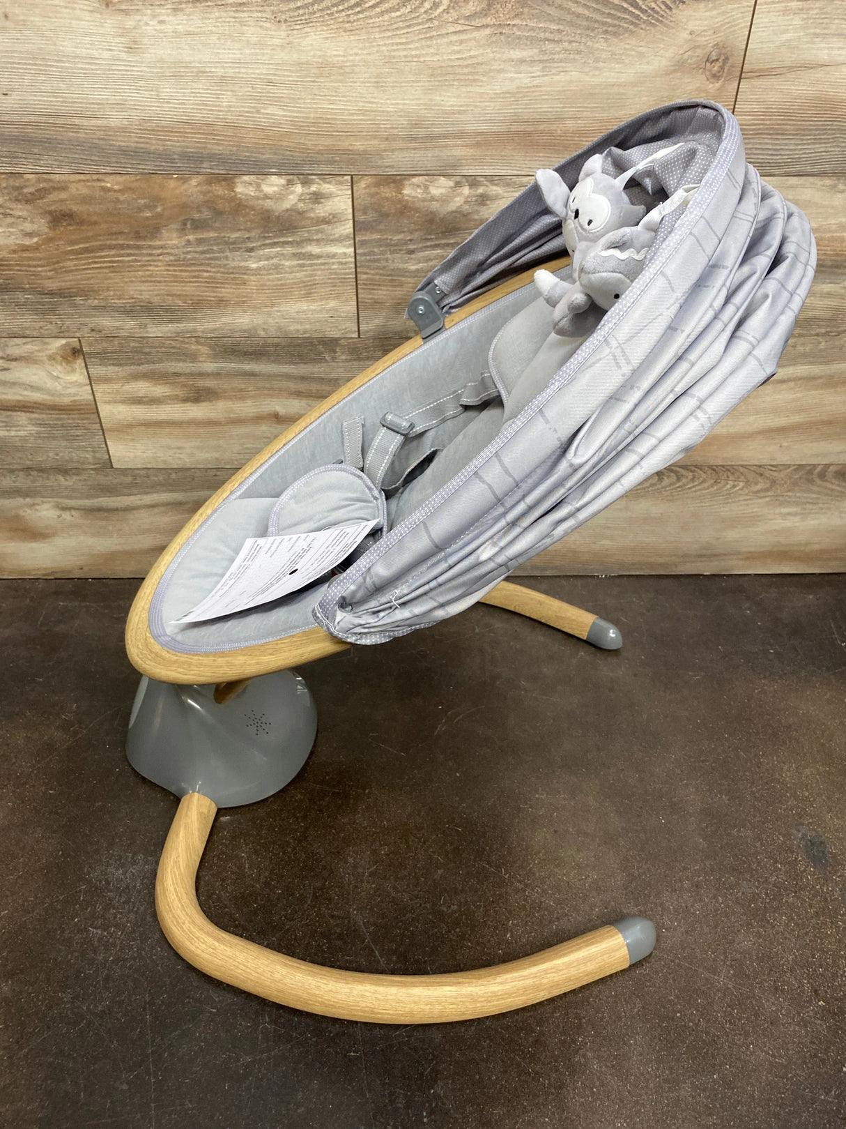 Angled view of Safety 1st 5-Modes Bluetooth baby swing with gray seat, plush toy bar, canopy, harness, and wooden base