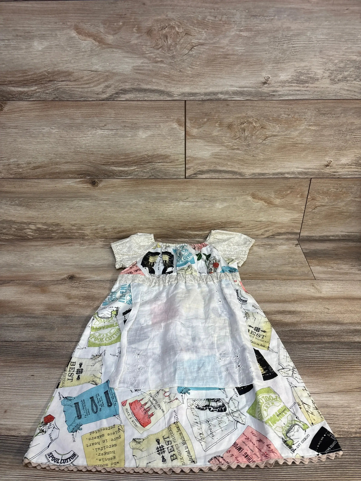 Vintage-style baby dress with sewing pattern print, short sleeves, and ruffled hem on wood floor
