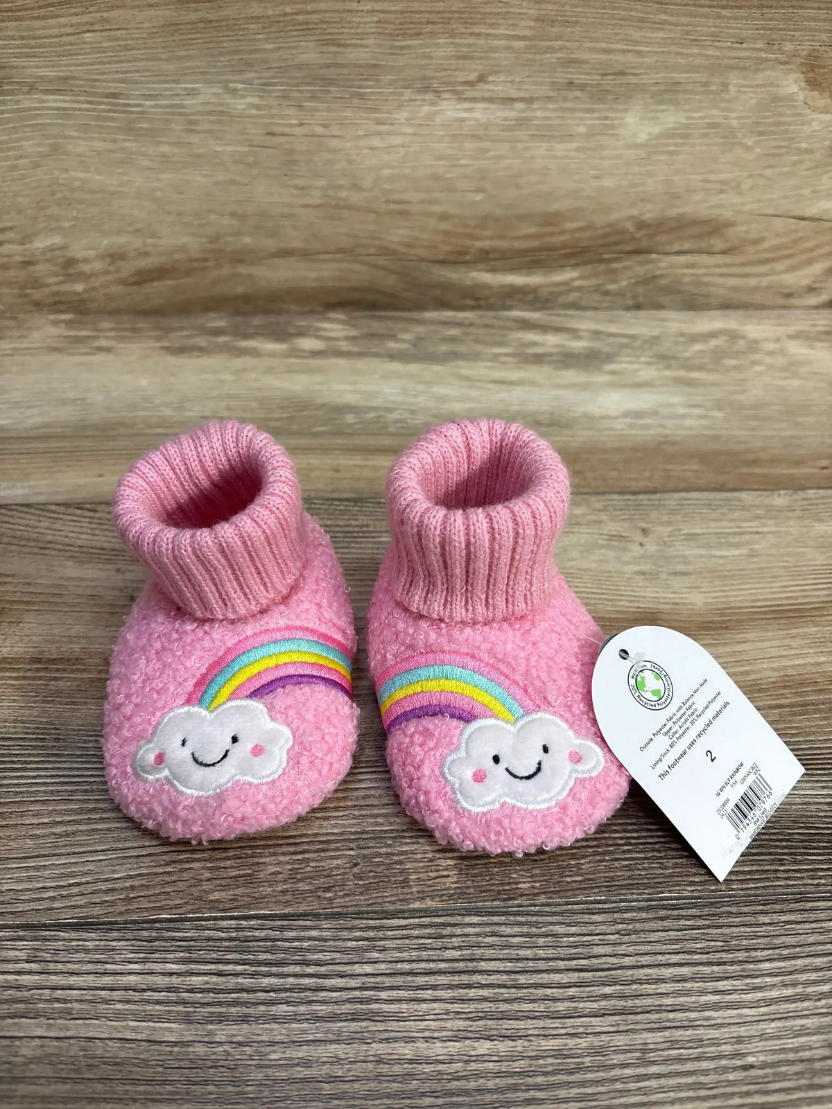 Pink baby booties with rainbow and smiling cloud design on wood background