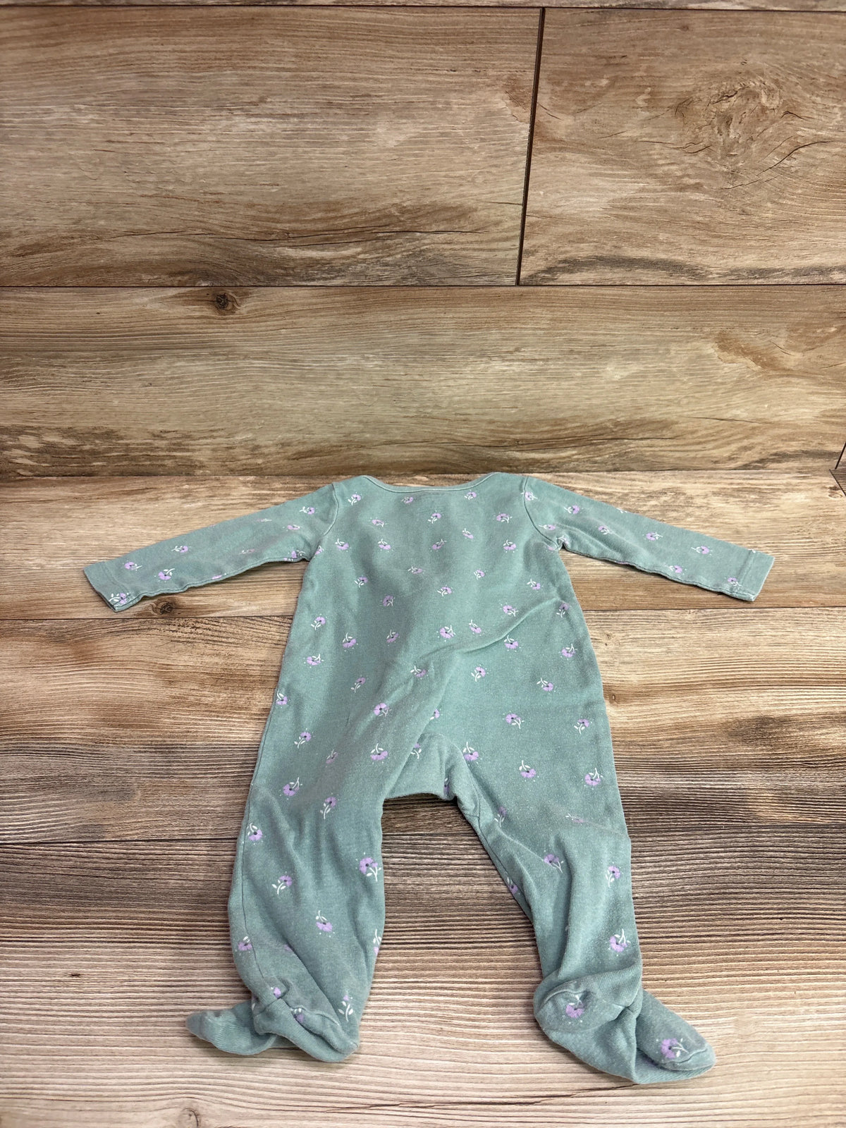 Top view of Just One You green sleeper in size 6m showcasing long sleeves, covered feet, and floral print on a wood surface