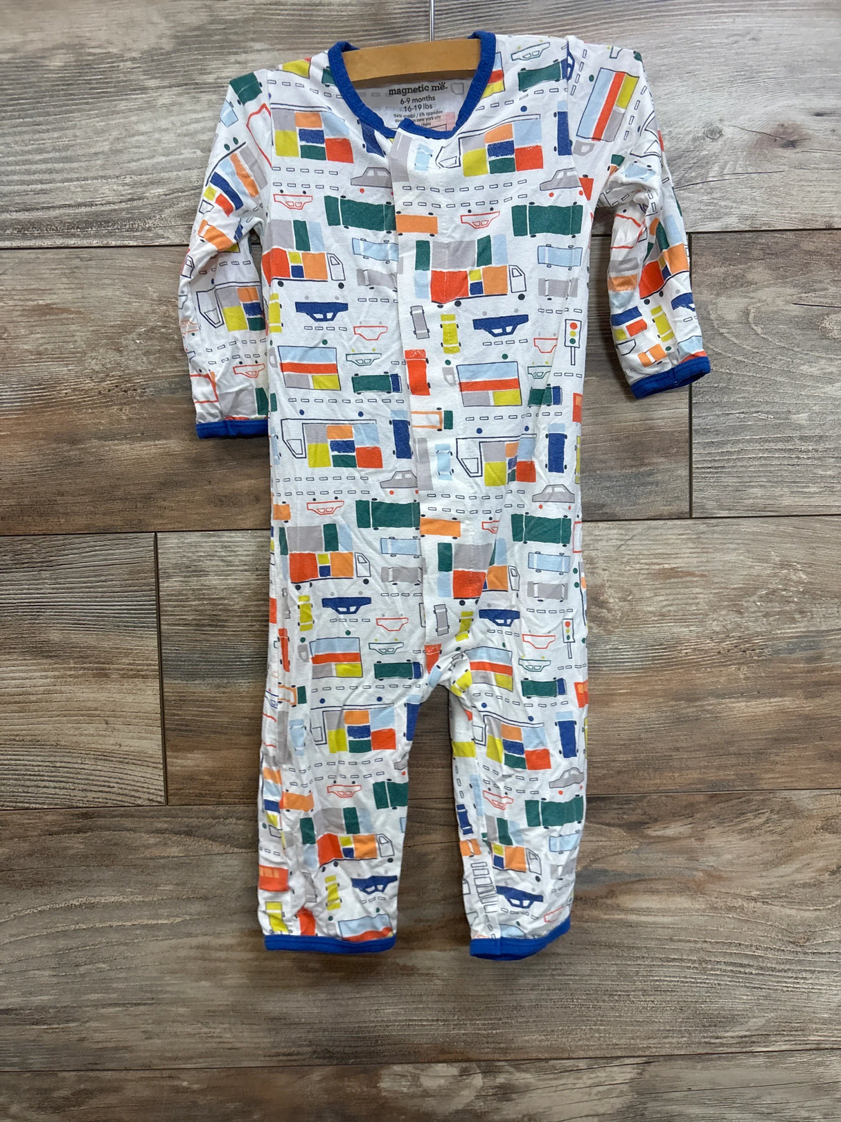 Front view of Magnetic Me modal footed sleeper, white with multicolor traffic vehicle print and magnetic front closure on wood floor