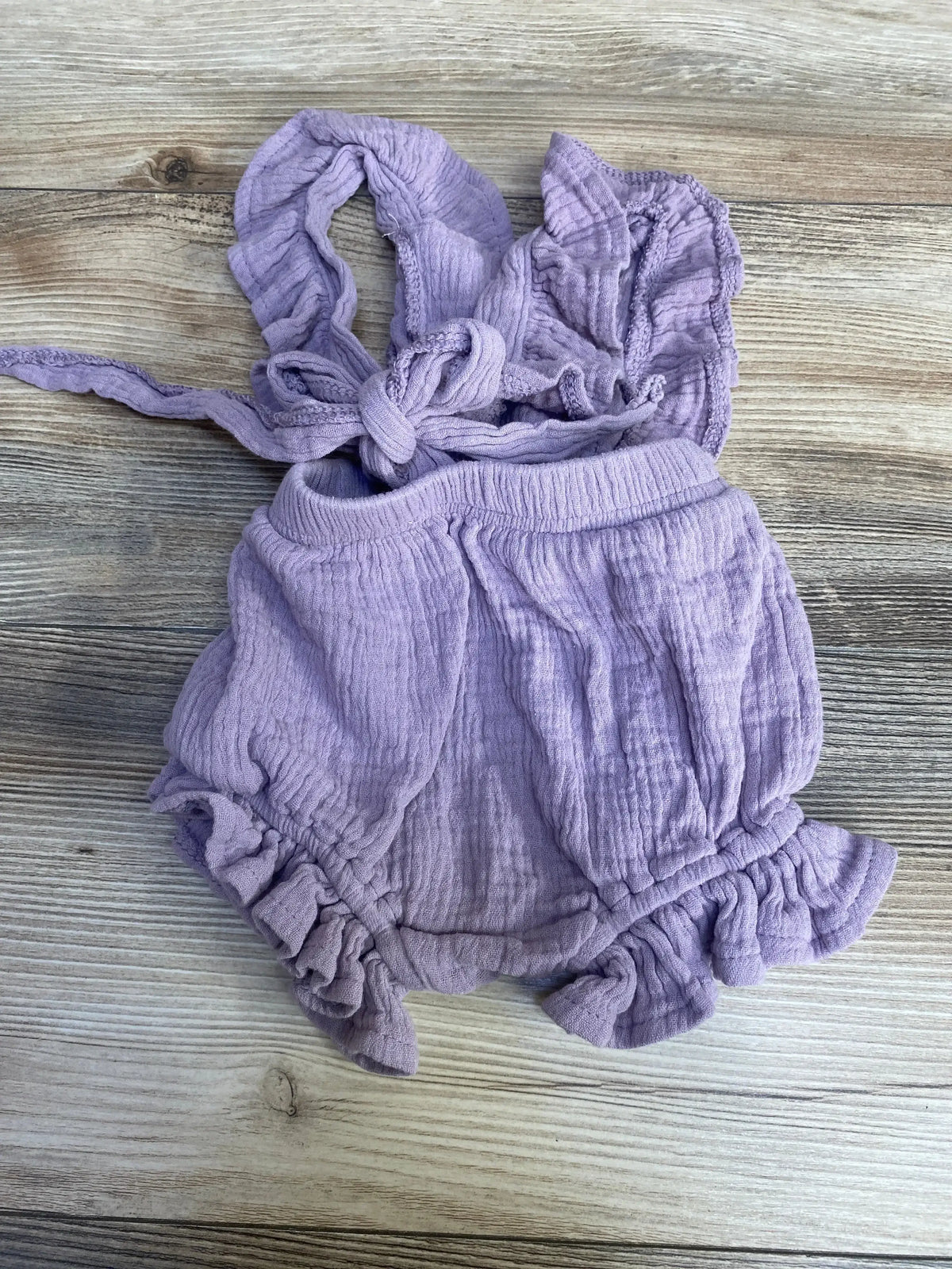 Flat lay of purple ruffle romper (3 months) showing tied shoulder straps and ruffled leg openings on light wood background